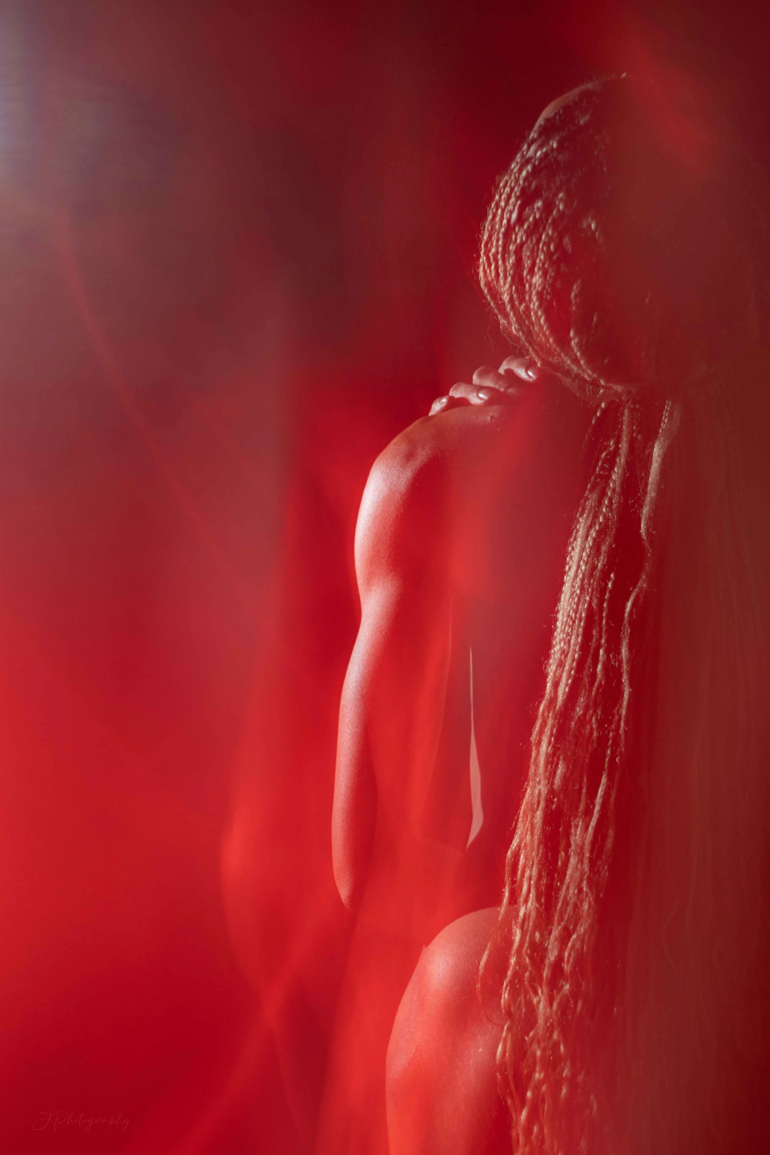 Une femme aux cheveux longs et tressés, vue de profil, avec un éclairage rouge chaud d'arrière-plan.