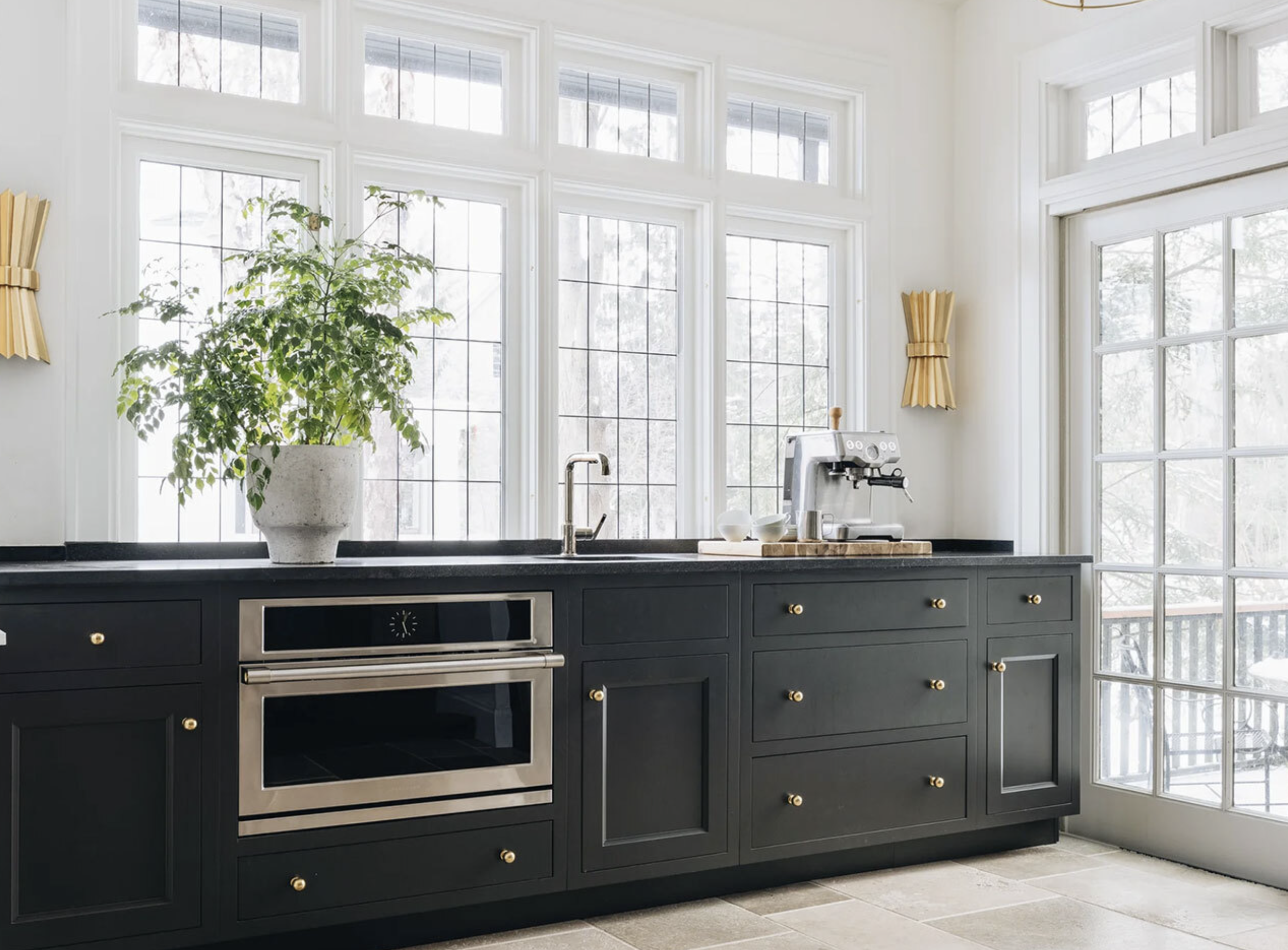 Kitchen with black cabinets, large windows, a potted plant, a coffee machine, and a door leading outside.