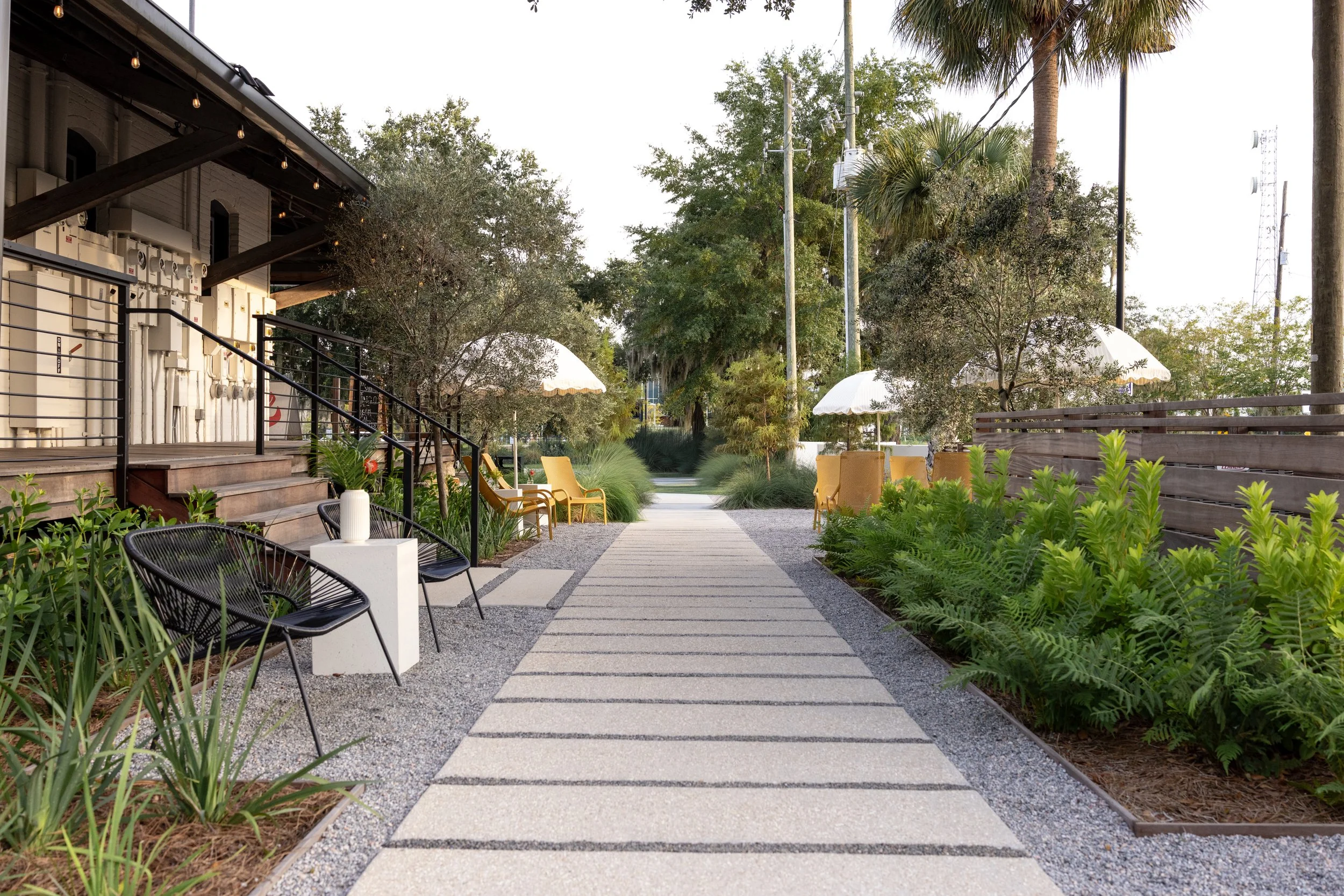 empty garden space with concrete path, chairs and umbrellas that comfortably fits 50-60 guests 