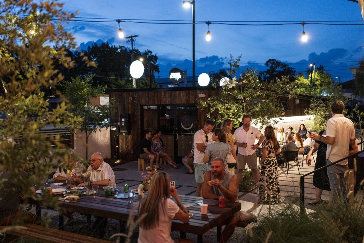  moodily lit dining area at night filled with people standing and seated at large picnic table. offers additional seating for large parties. 