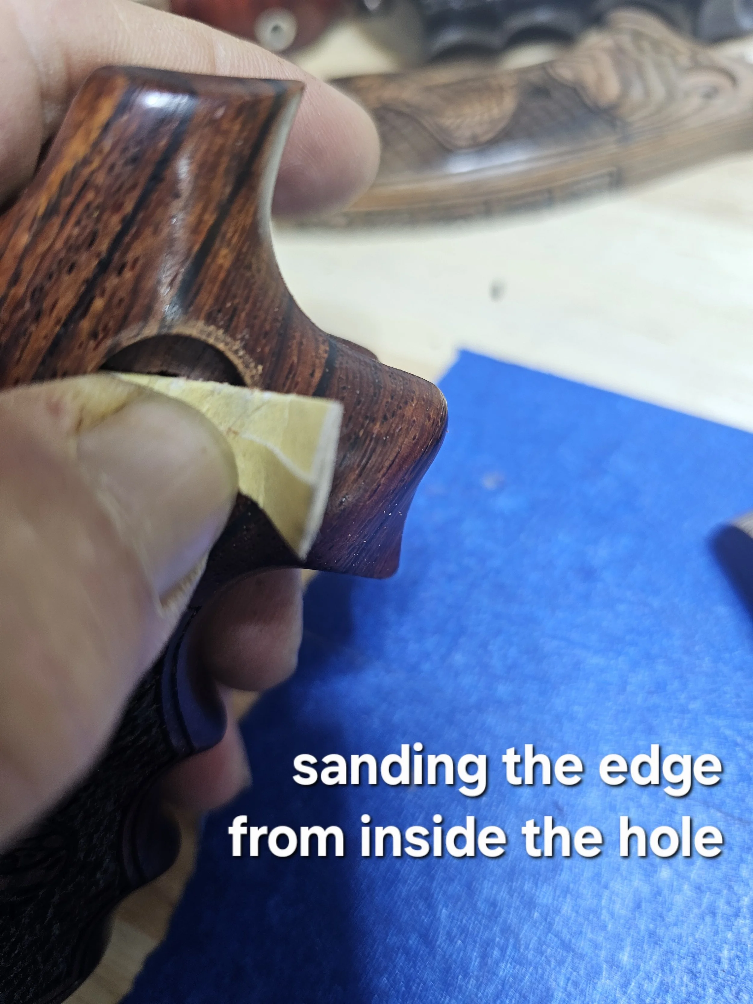 Close-up of a person sanding the edge of a wooden object from inside the hole.