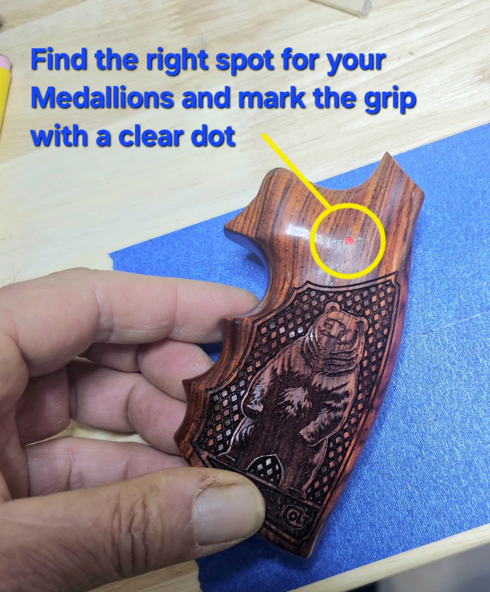 Close-up of a person's hand holding a wooden firearm grip with intricate carvings, pointing toward a wooden surface with a yellow dot marked on it for a target.