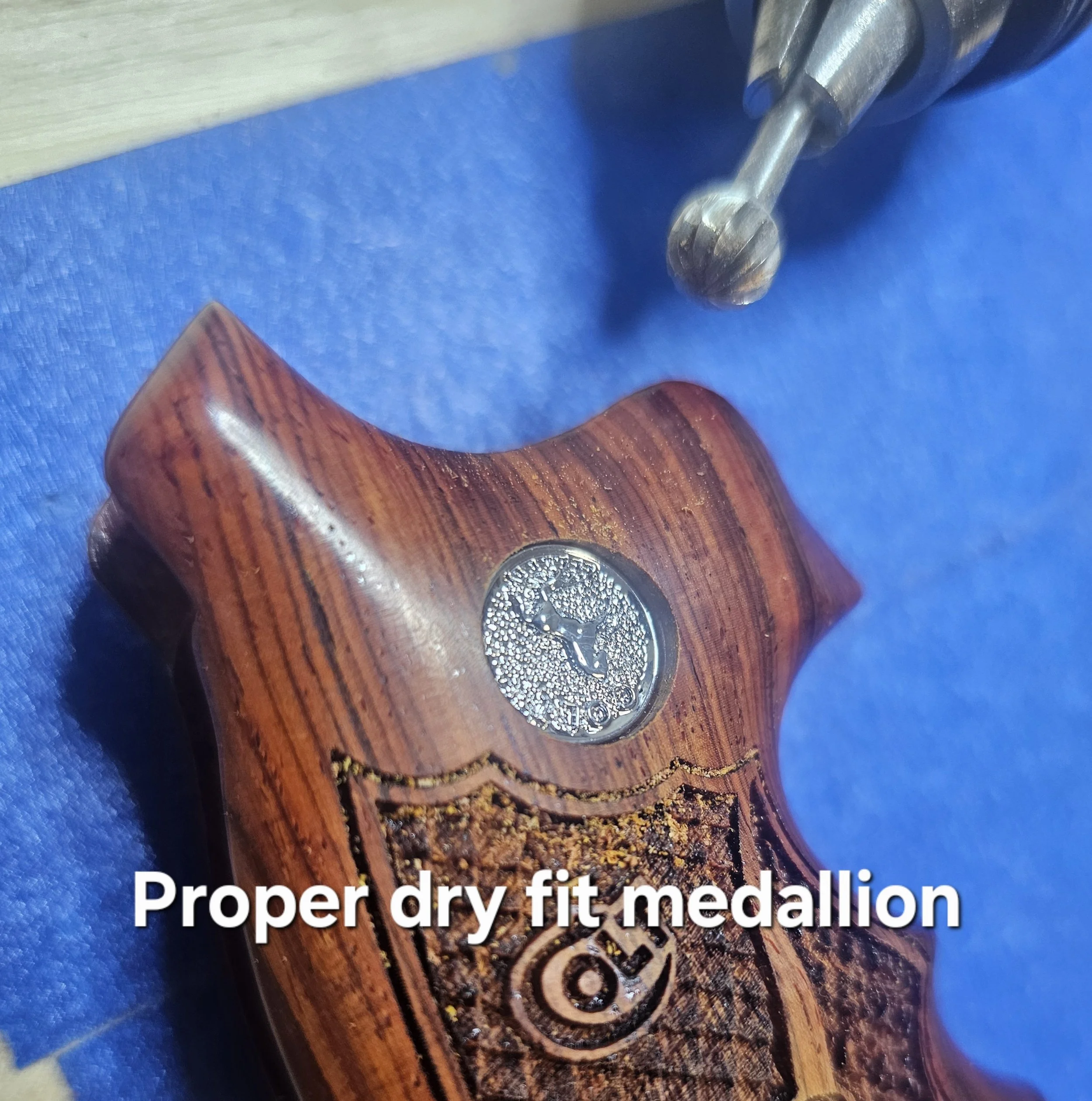 Close-up of a metallic medallion embedded in a wooden surface with intricate designs, and English text partially visible at the bottom.