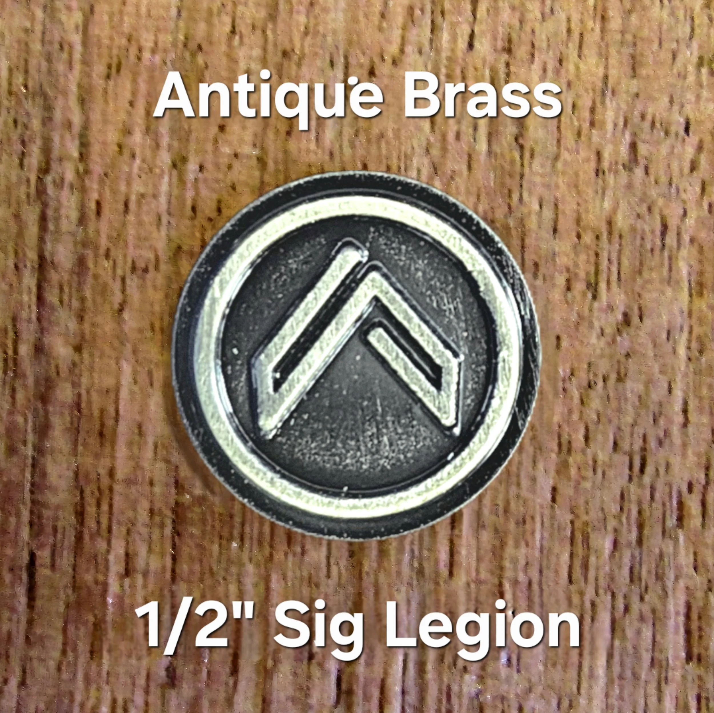 Close-up of a vintage brass badge with the text '1/2" Sig Legion' placed on a textured wooden surface.