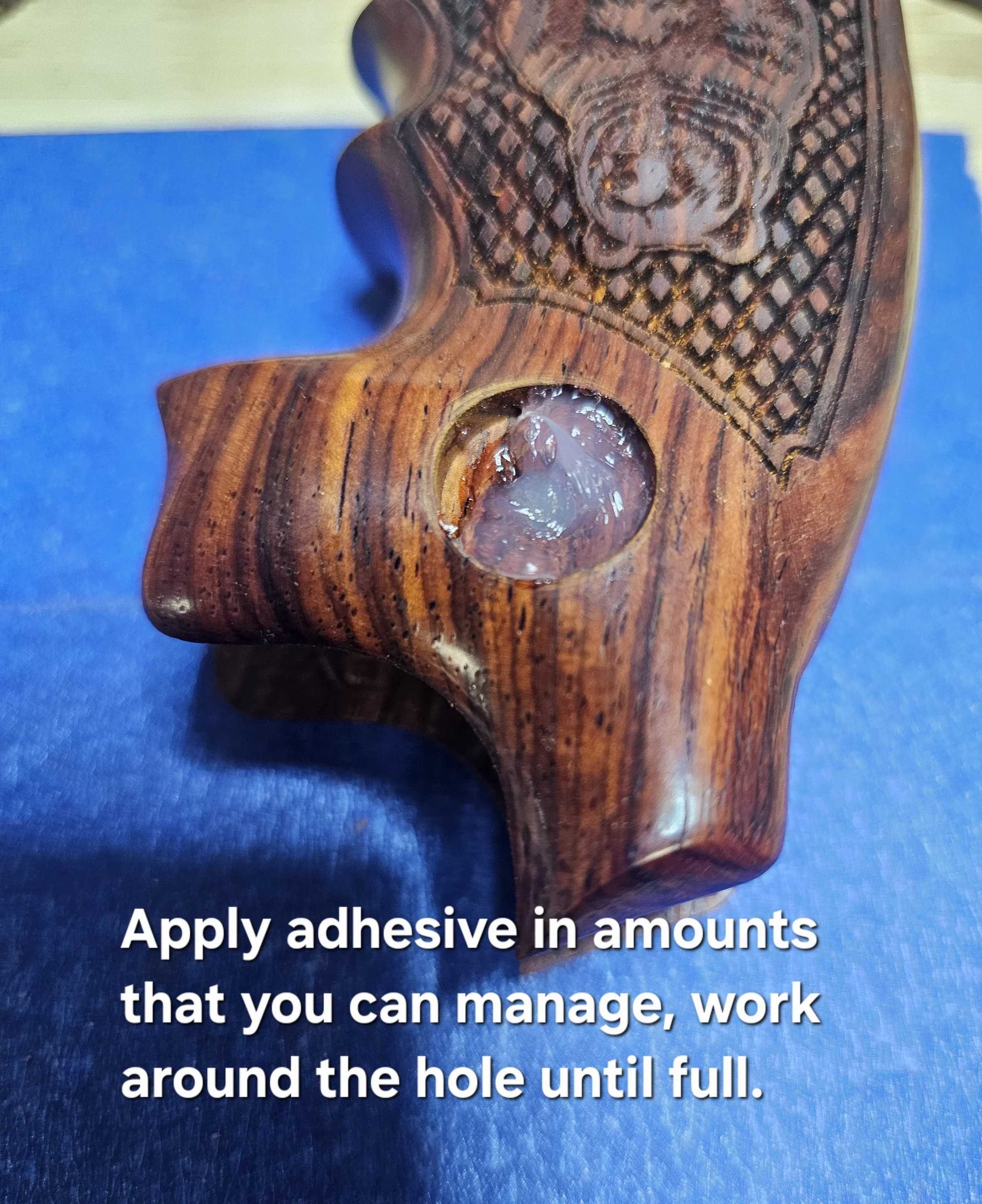 Close-up of a wooden object with a carved lion or similar animal face, with a hole and adhesive visible, on a blue background. Part of a caption with instructions to apply adhesive in amounts that can be managed, work around the hole until full.