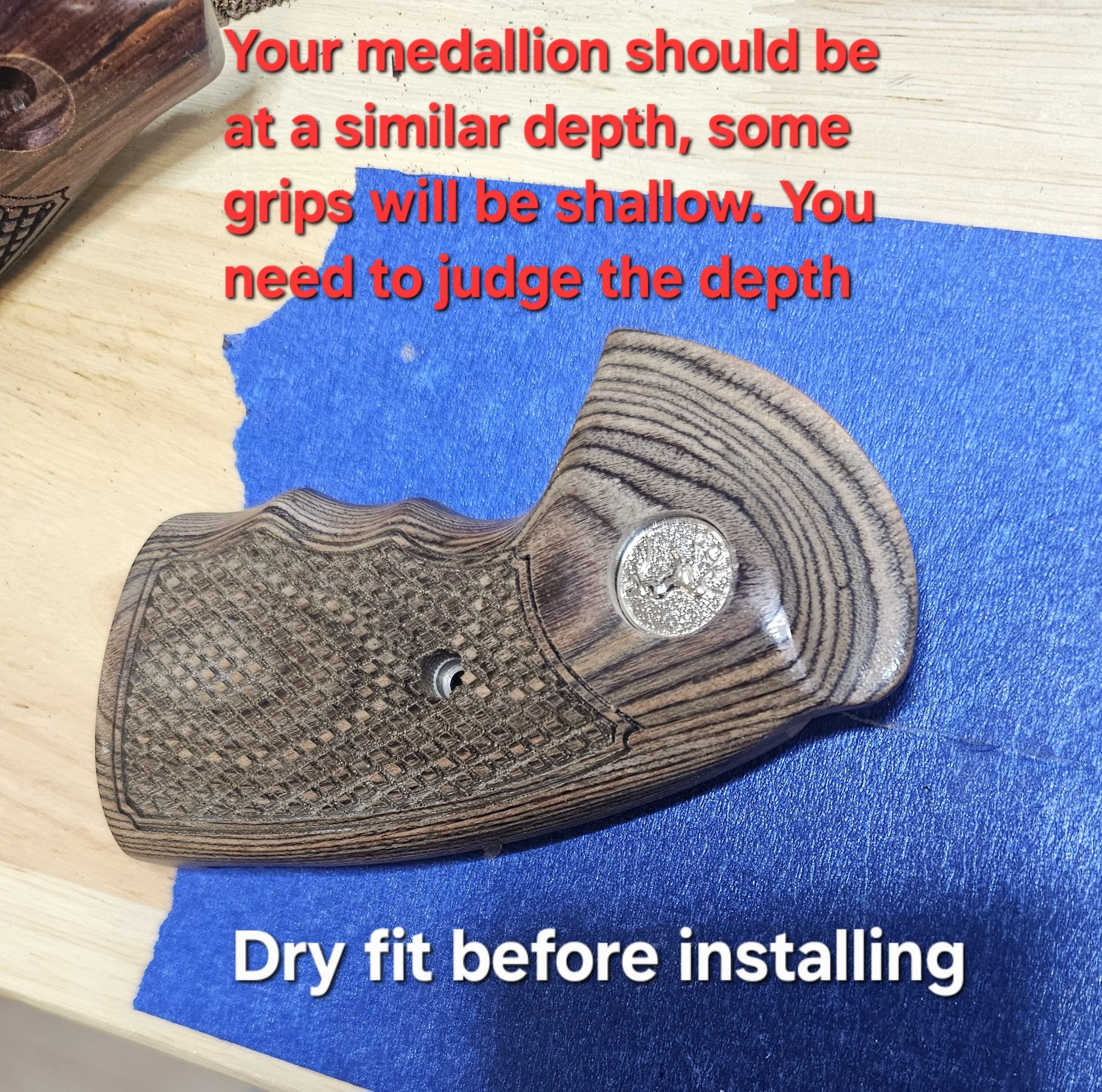 Close-up of a woodworking project with a wooden piece, blue painter's tape, and printed instructions about installing Medallion. The text on the tape reads, 'Dry fit before installing,' and the partial instruction overlay says, 'Your medallion should be at a similar depth, some grips will be shallow. You need to judge the depth...'