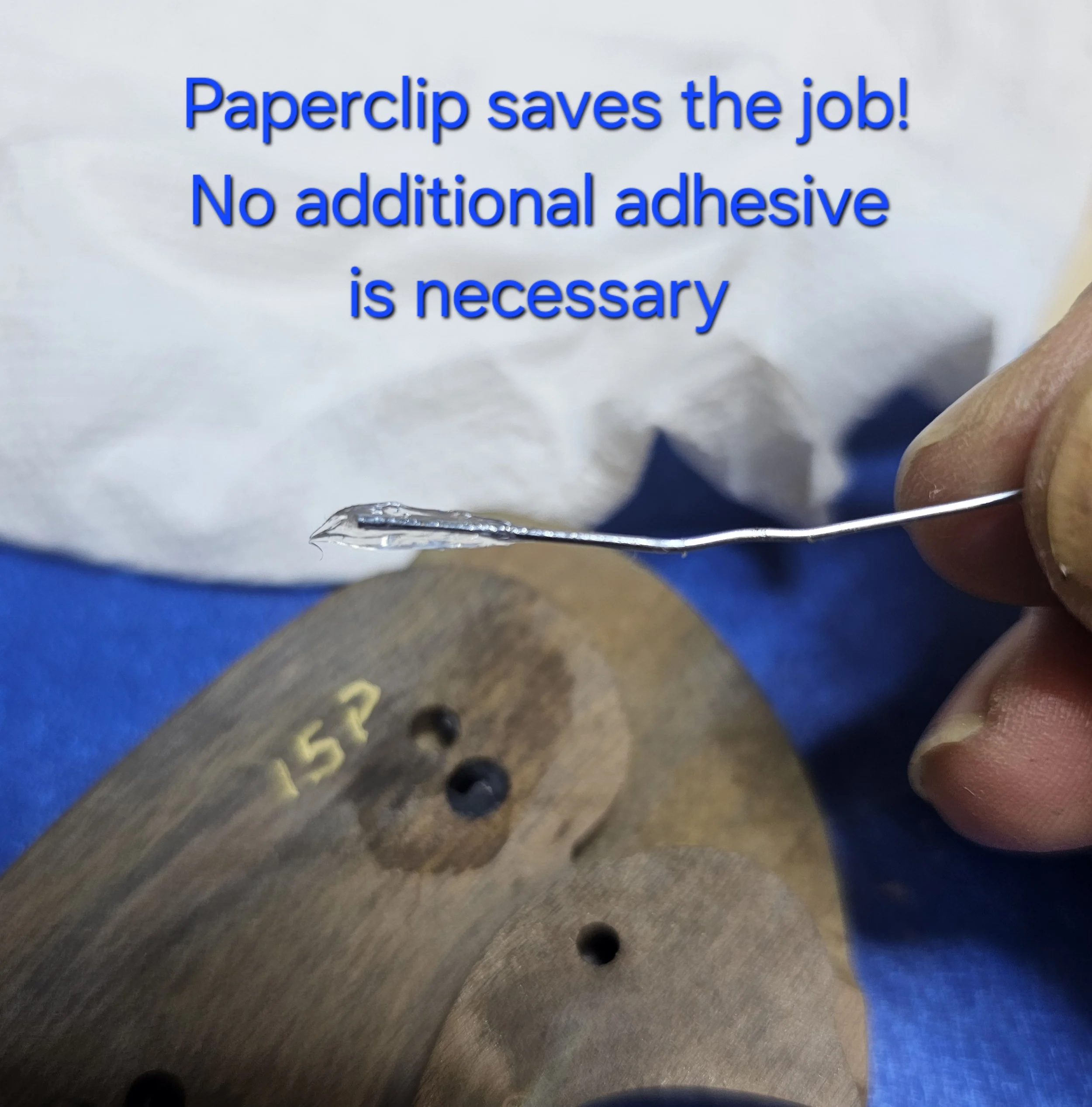 Close-up of a sign that reads 'Paperclip saves the job! No additional adhesive is necessary,' being held by a person's hand.