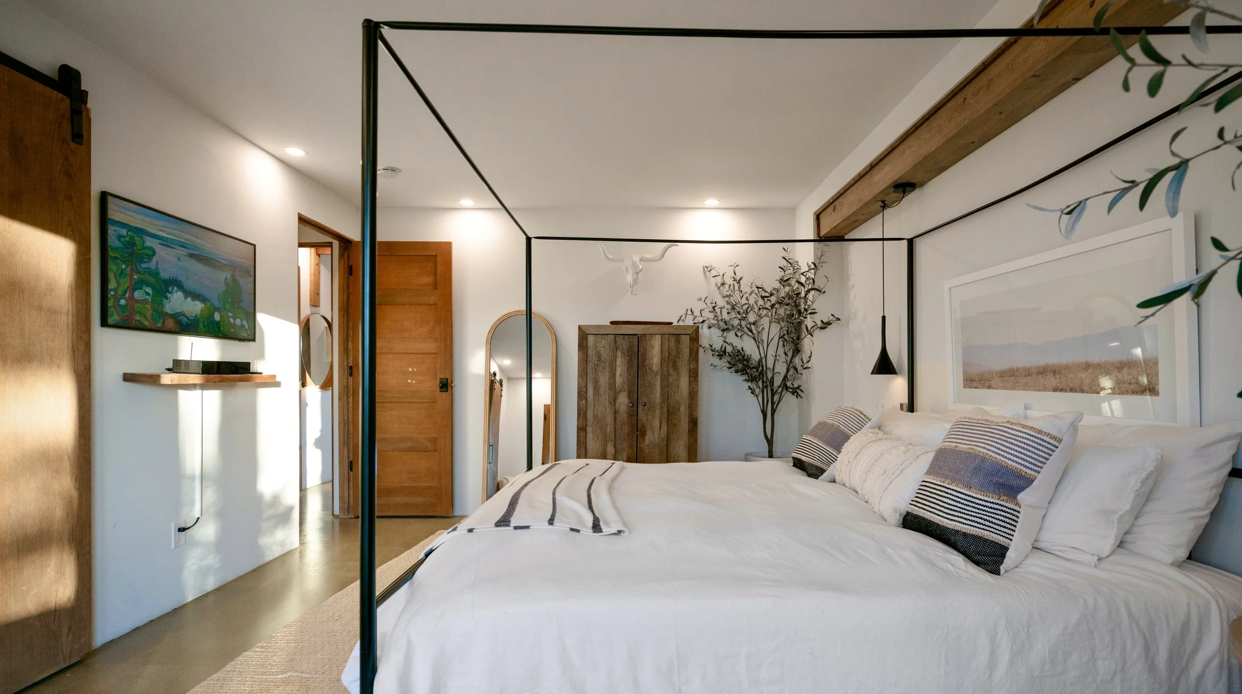 Side view of the Primary Bedroom with the king canopy bed, wall-mounted TV, wooden storage cabinet, and doorway to the home.
