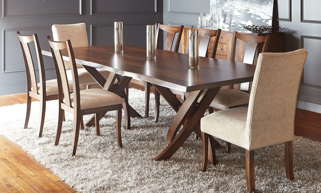 Wood dining table with eight chairs, four upholstered with beige fabric and four wooden, in a room with gray paneled walls, a rug, and decorative items on a sideboard, along with a large window showing a snowy landscape.