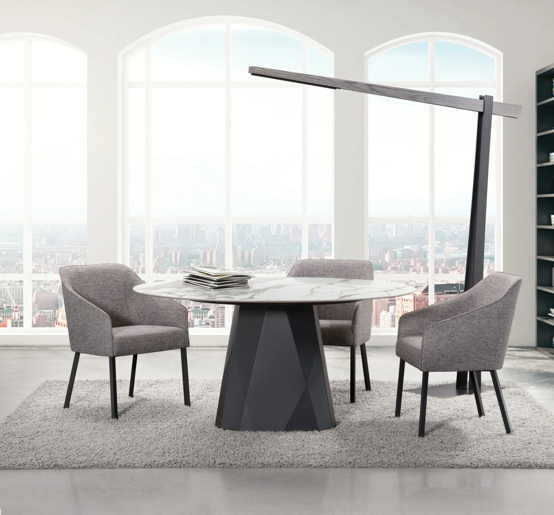 Modern office meeting room with three gray chairs around a round marble table, a stack of papers on the table, large windows showing a city skyline, and a standing lamp.
