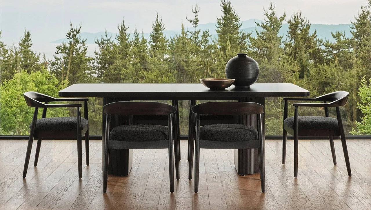 Dining room with a black table, five black chairs, and decorative vases on the table. Large window showing a view of green trees outside.