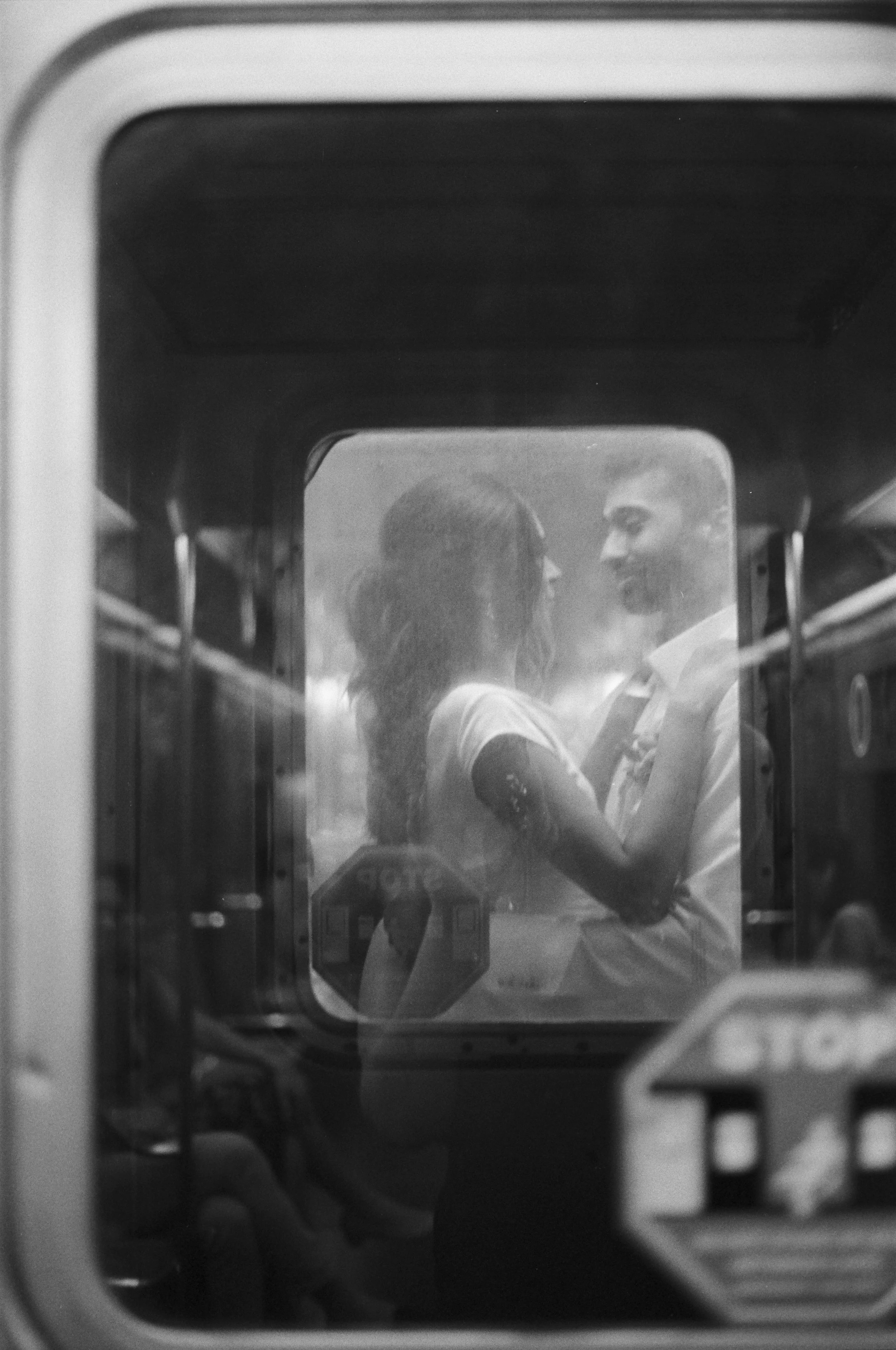 A black-and-white photo of a couple looking at each other through a subway window in NYC