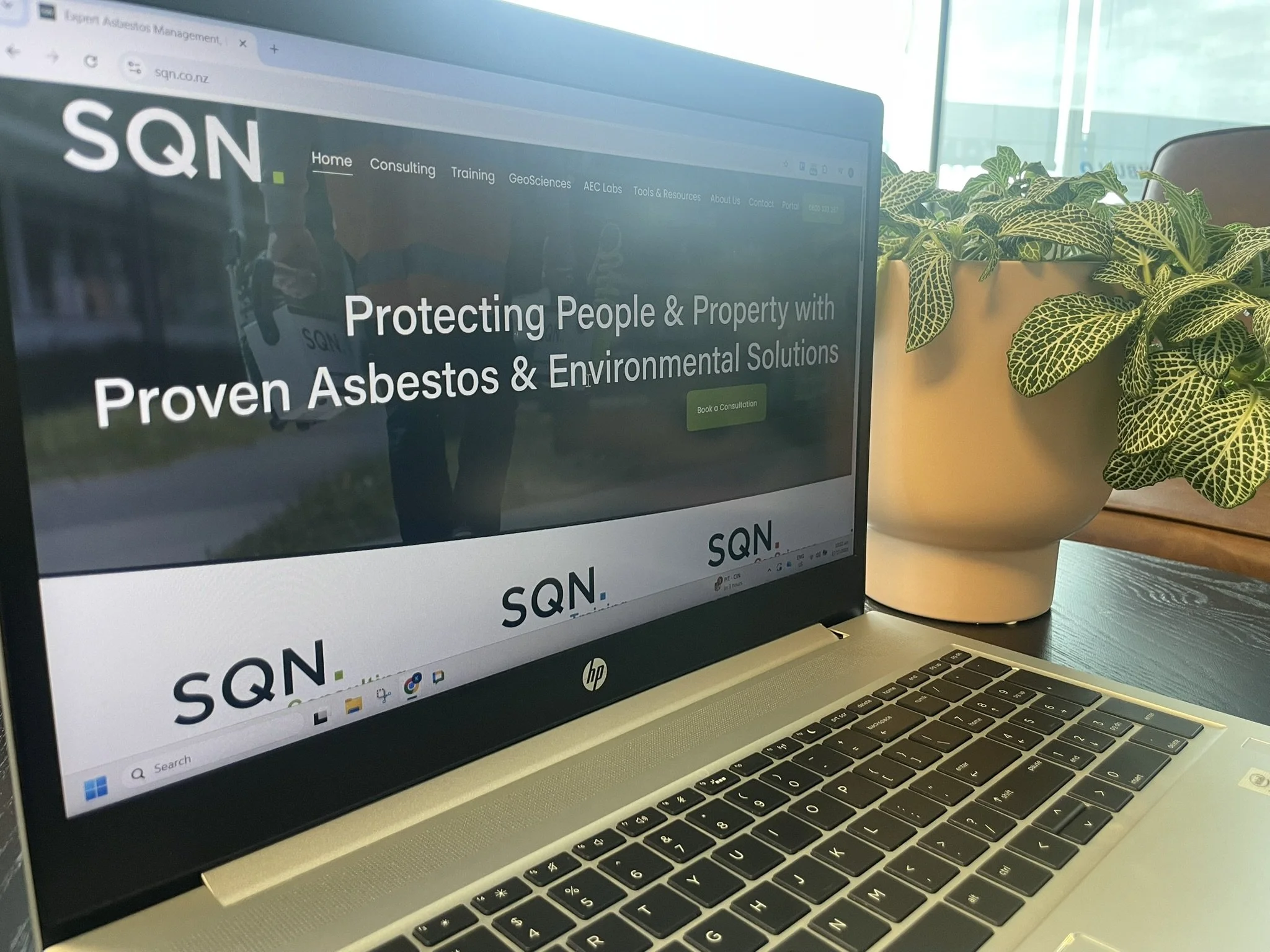 Laptop on a table displaying a website for SQN, a company that provides asbestos and environmental solutions, next to two potted plants.
SQN Consulting, SQN Training, SQN GeoSciences