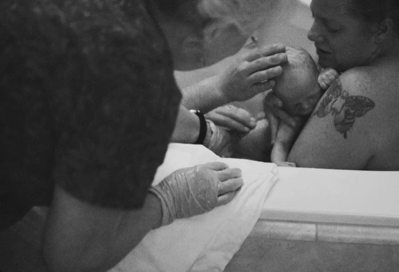 A woman giving birth in a birth center tub, with midwife assisting