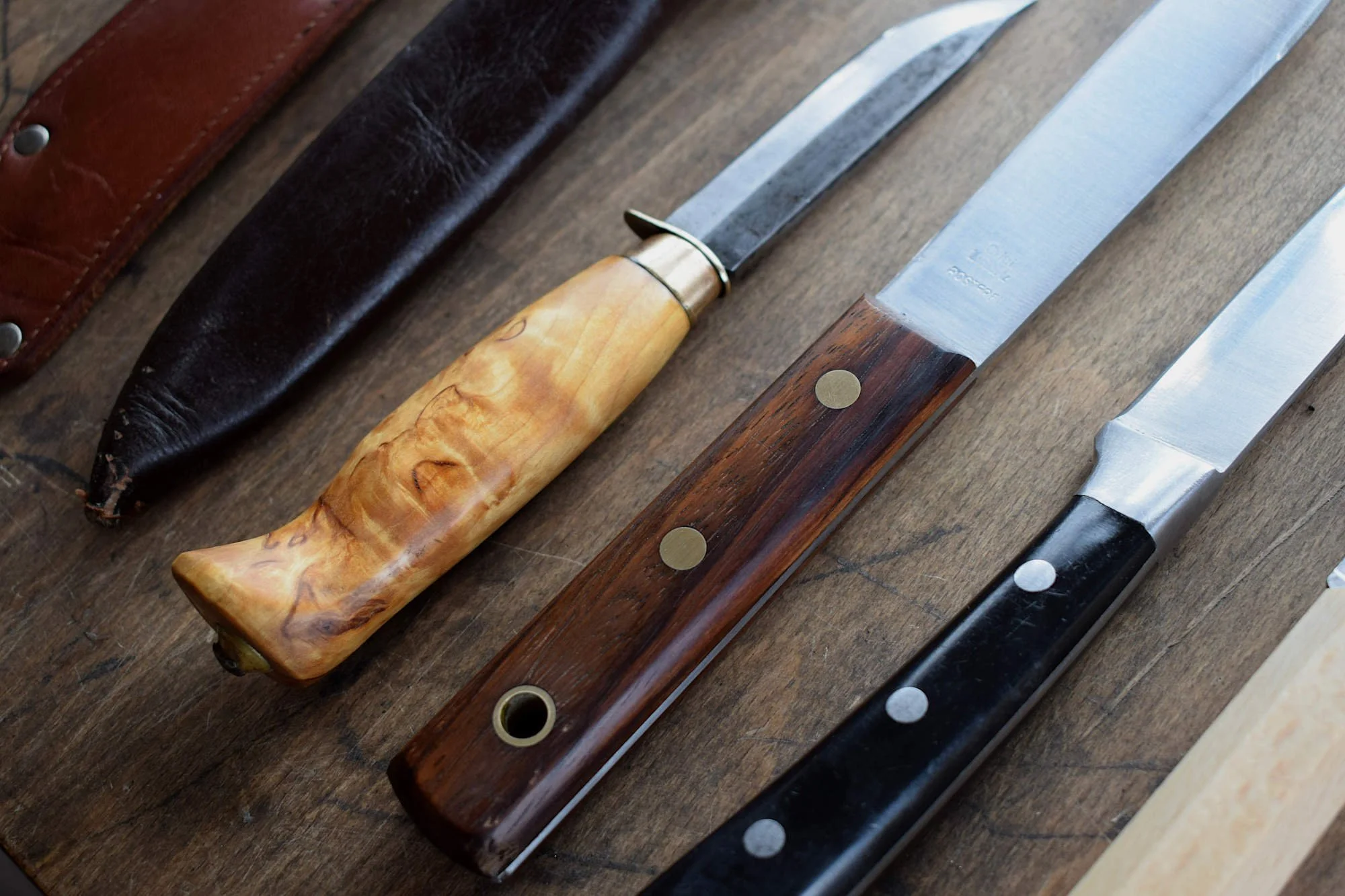 Assortment of knives with wooden and metal handles on a wooden surface.