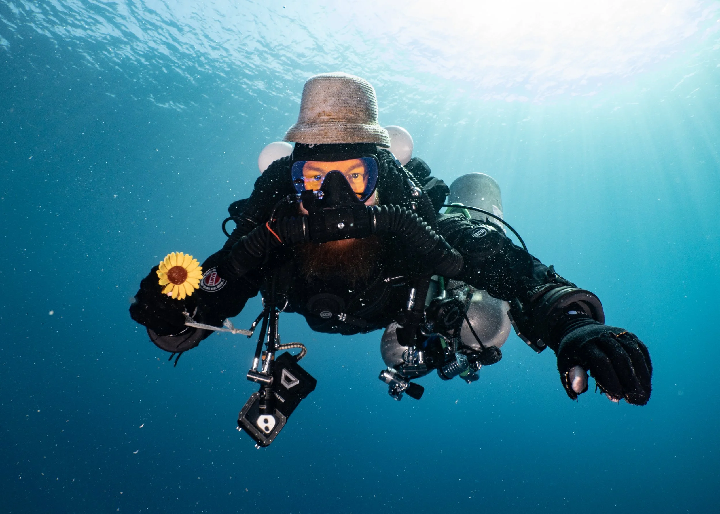Technical diver holding a yellow flower during a decompression stop in open water.