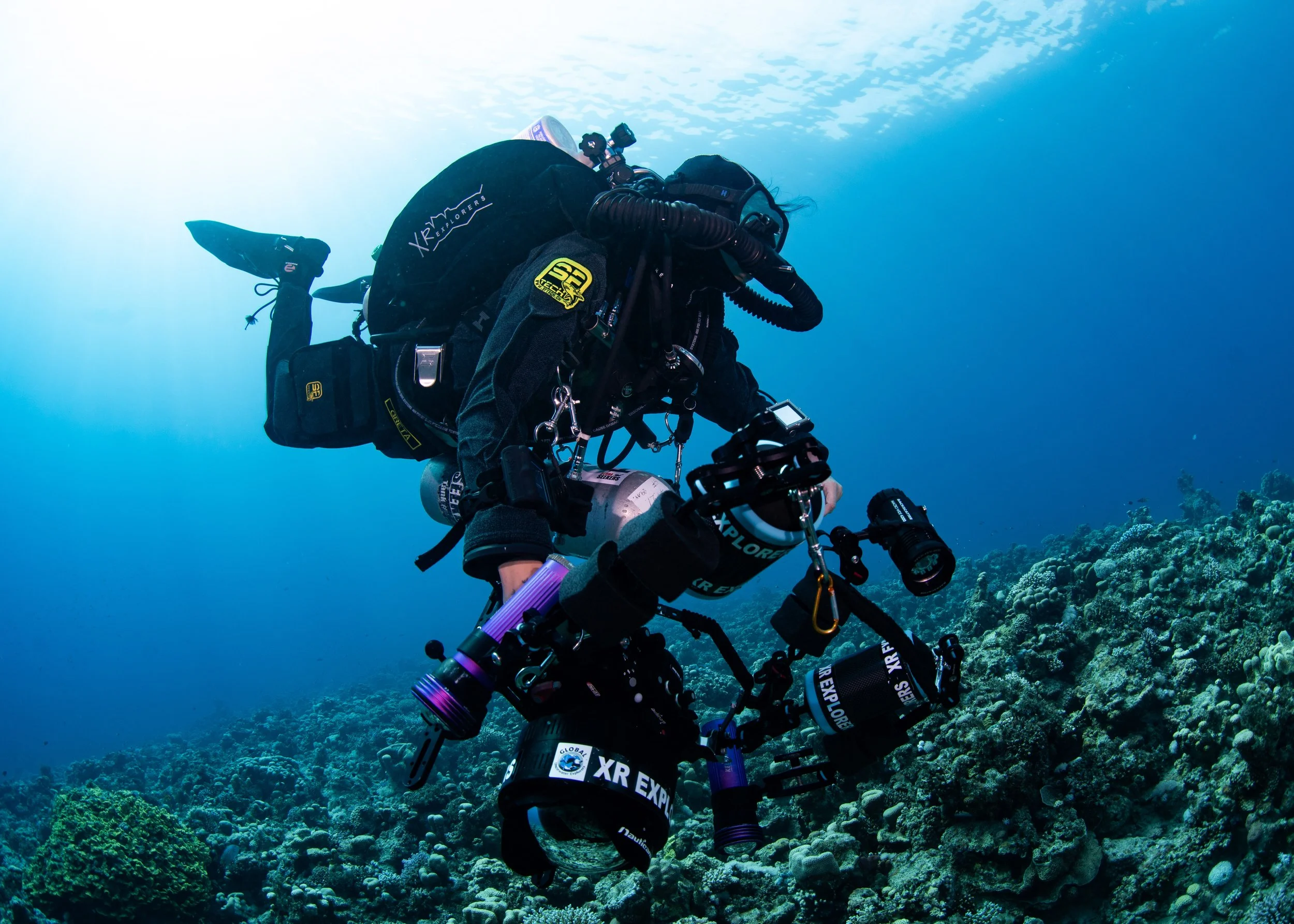 Female technical diver filming with underwater camera while performing a decompression stop on a GUE JJ rebreather.