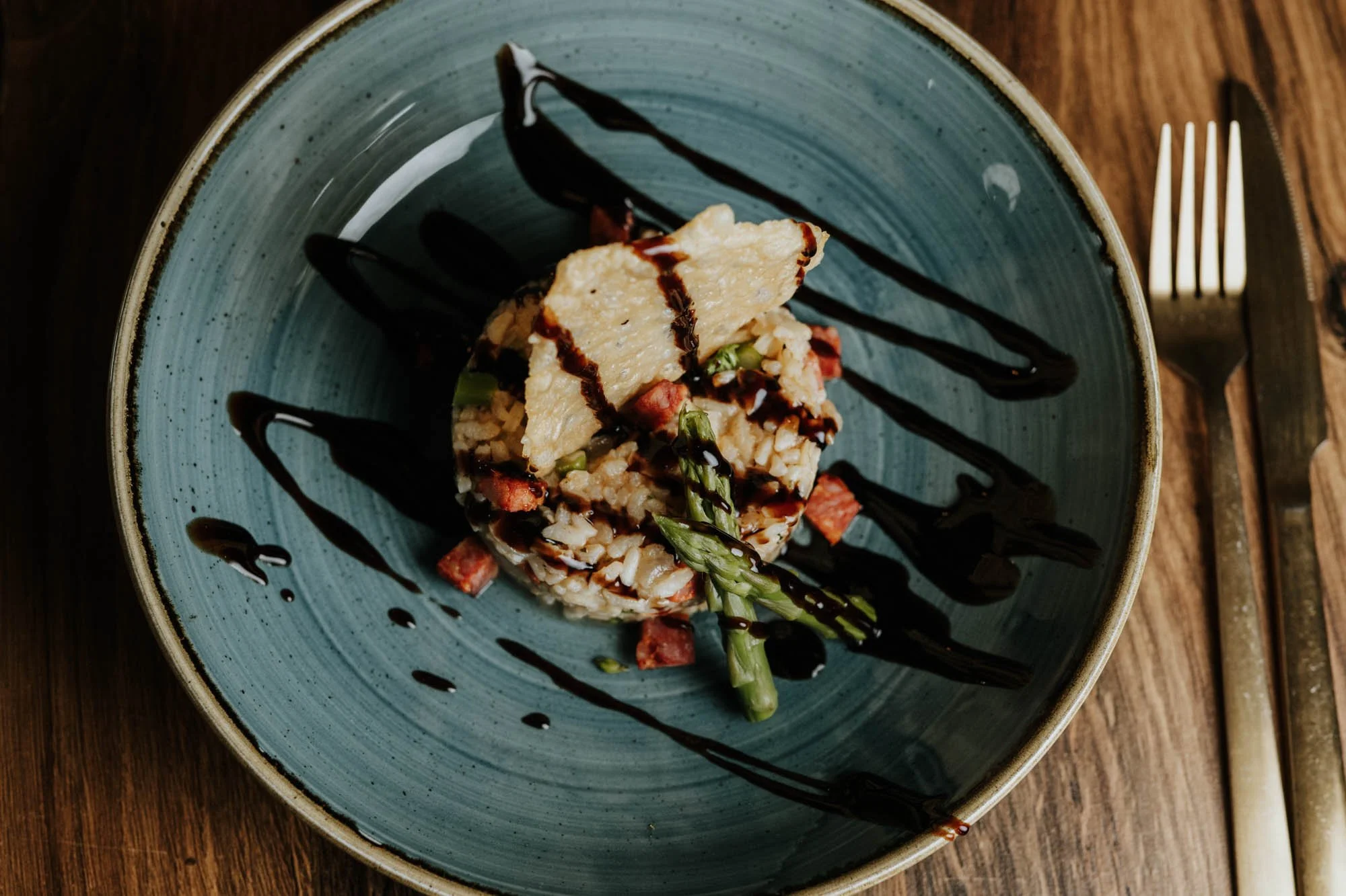 A plate with rice, grilled chicken, asparagus, bacon pieces, and a drizzle of balsamic glaze.