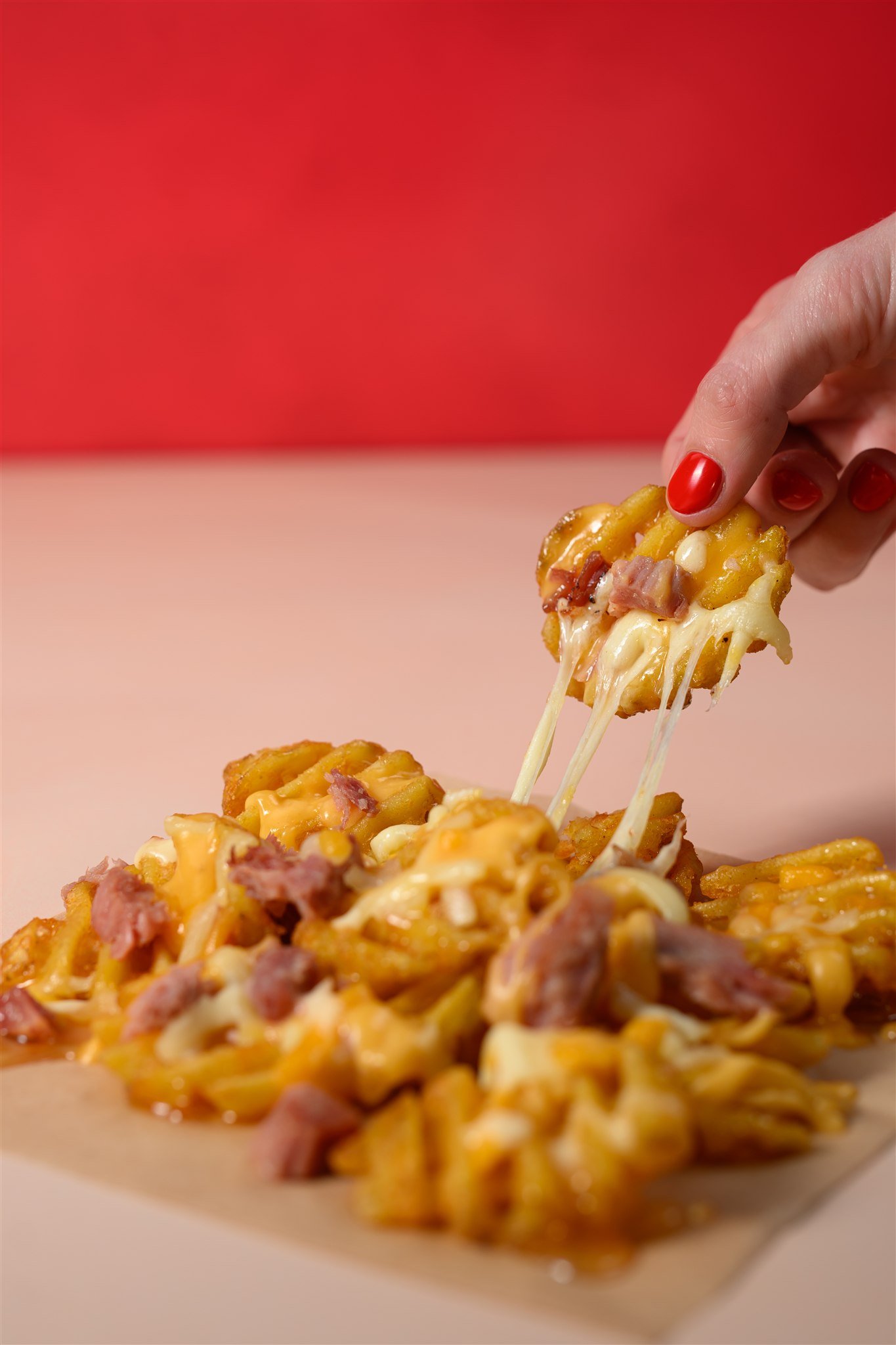 A hand with red painted nails lifting a cheesy, pepperoni and ham loaded cheesy bread from a tray.
