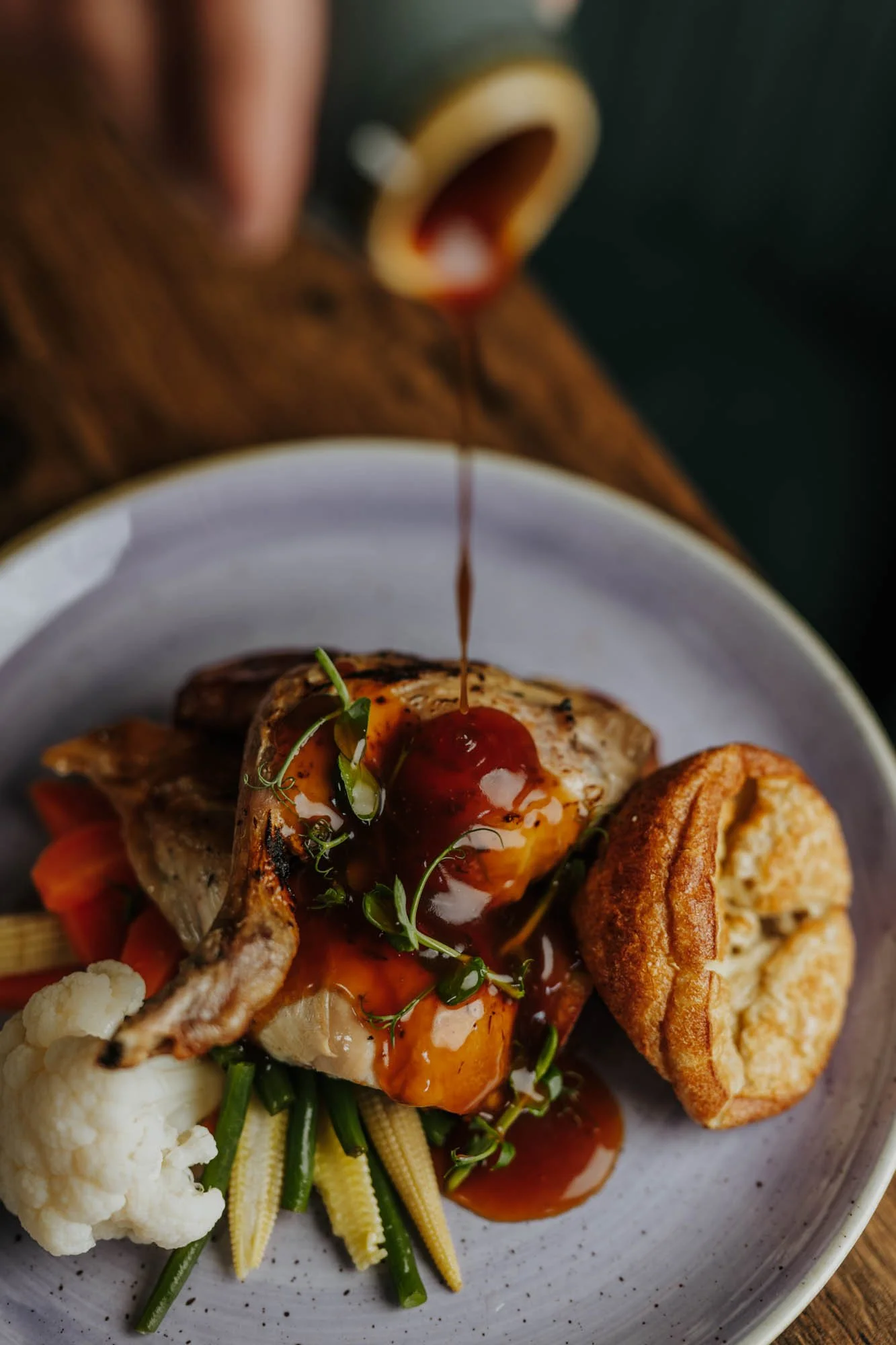 A plate of food with a filet of fish topped with sauce and herbs, served with cauliflower, green beans, baby corn, and a fried biscuit.