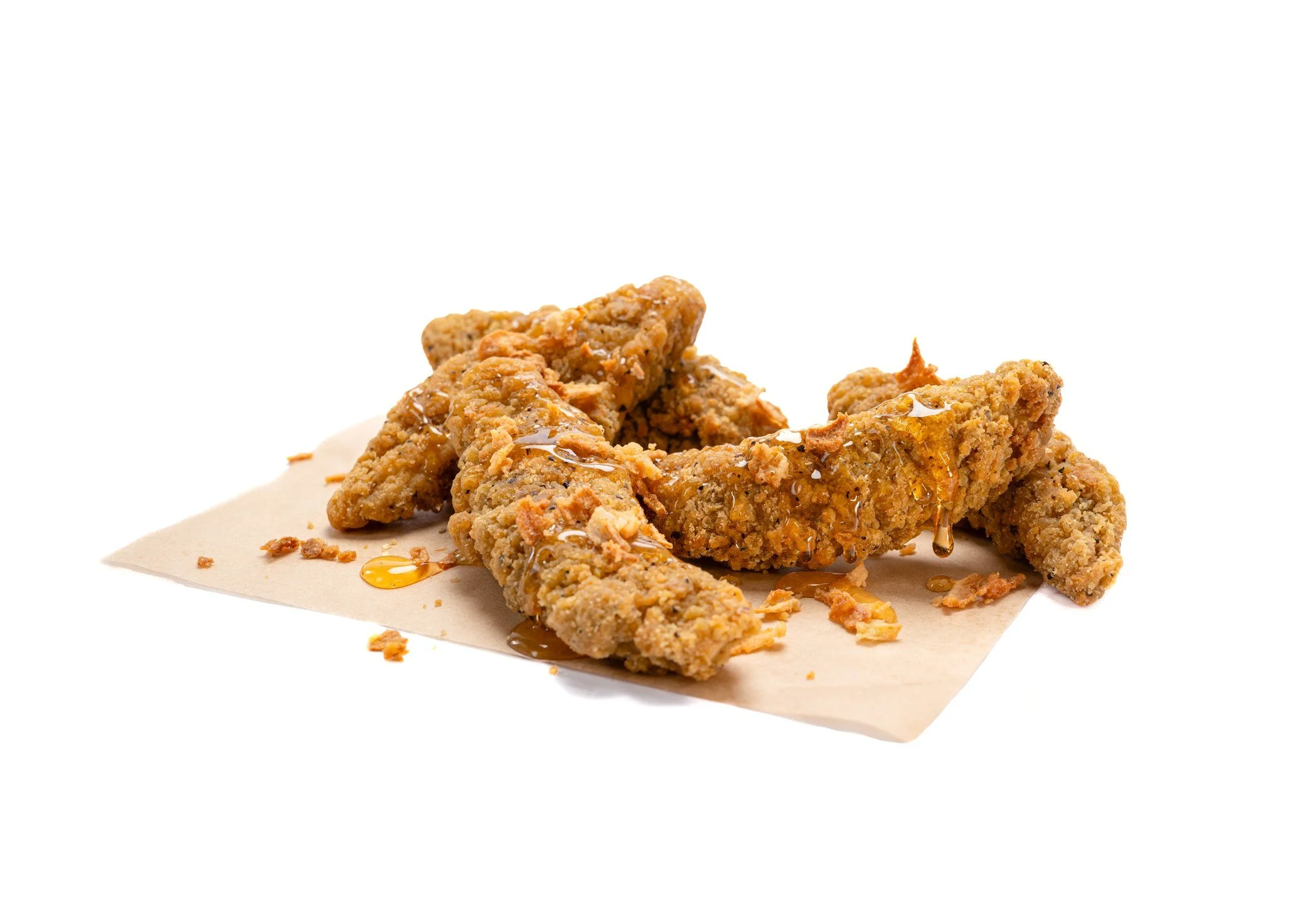 Fried chicken tenders with honey drizzle on parchment paper.