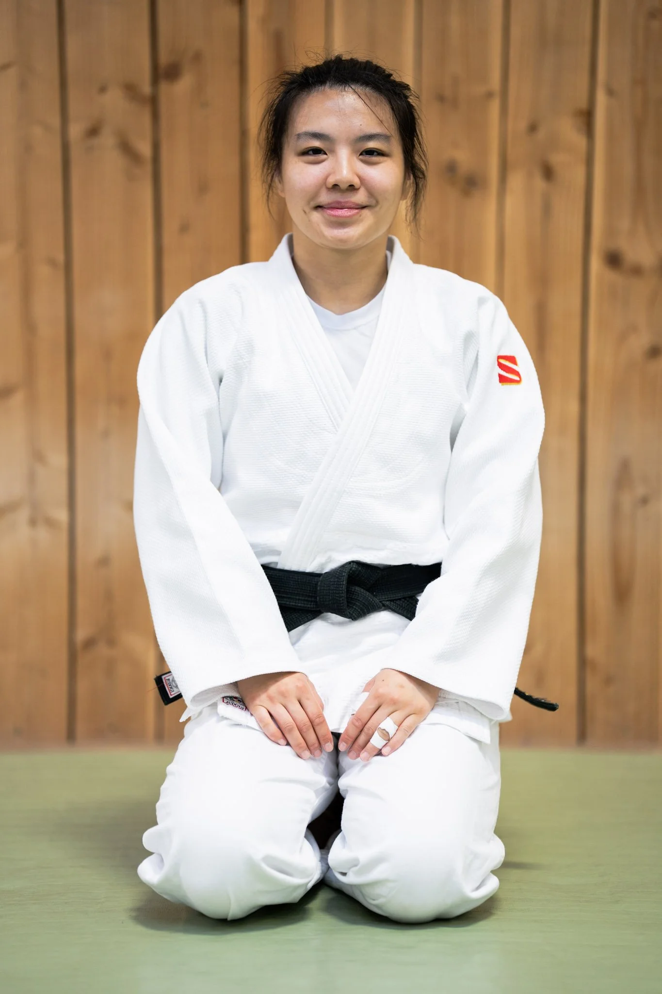 Young woman in a blue Brazilian Jiu-Jitsu gi standing in front of a wooden wall, smiling at the camera.