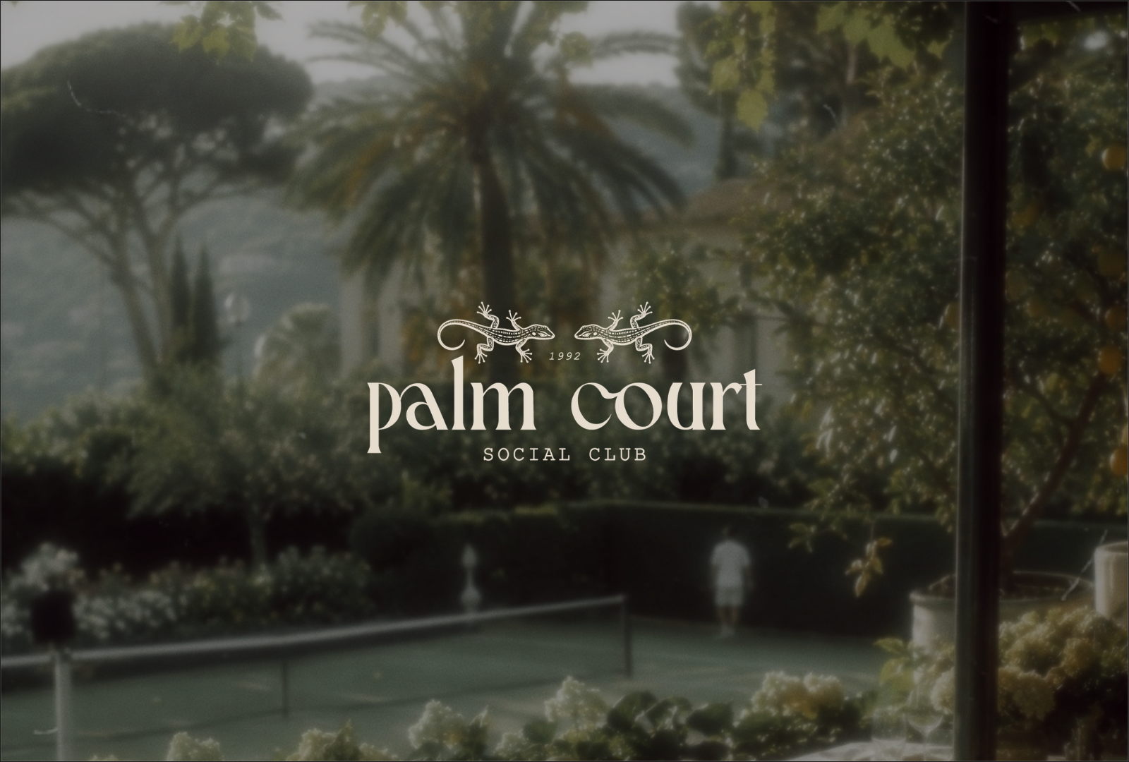 Outdoor view of Palm Court Social Club sign, with trees, plants, tennis court, and a person in the background.
