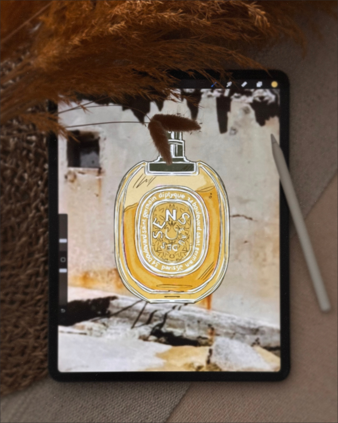 A tablet displaying an artistic illustration of a perfume bottle, with a brown fluffy plant partially covering the top of the screen. The background of the display shows a textured wall and stone surface, with a white stylus resting nearby.