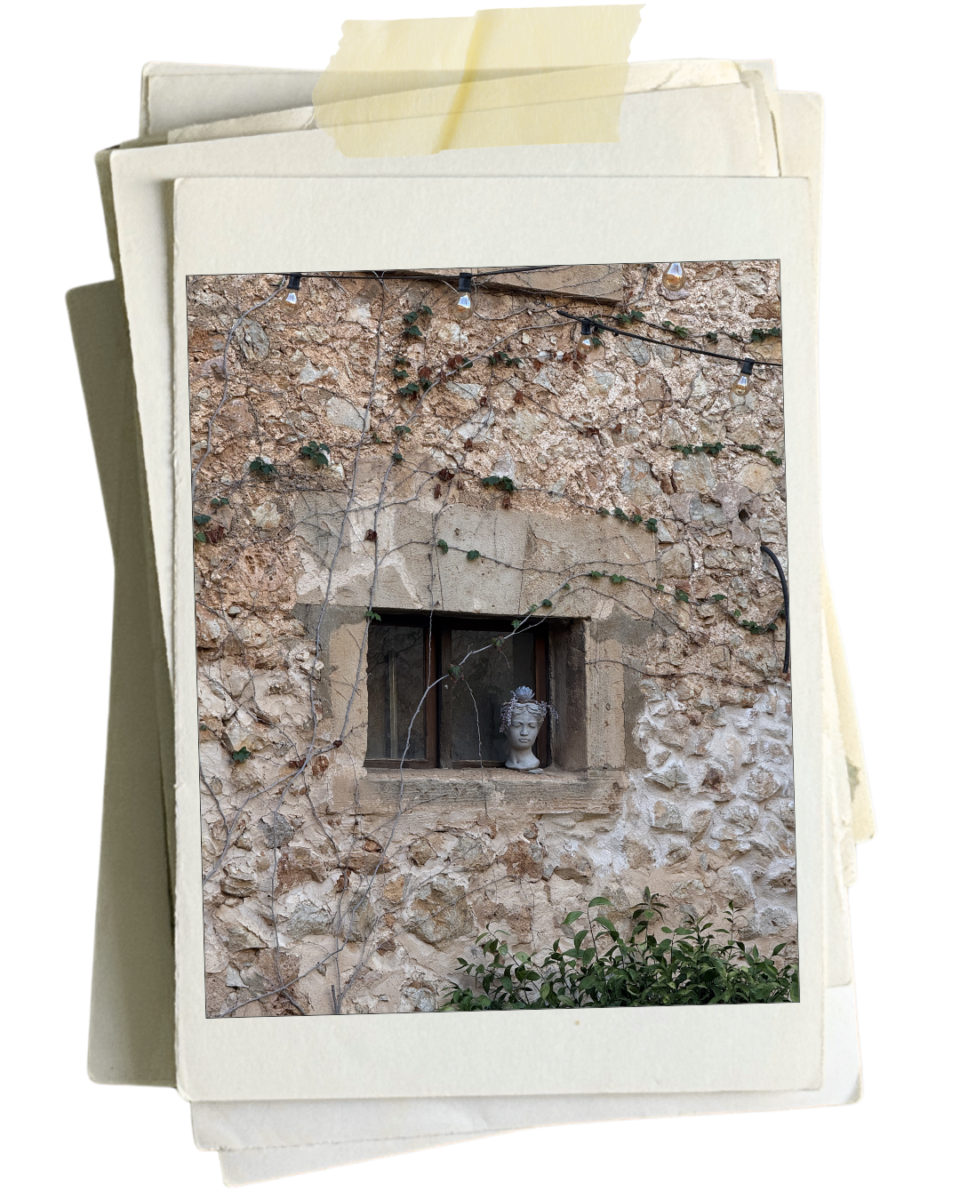 A stone wall with a small rectangular window, a decorative bust in the window, and string lights draped above.