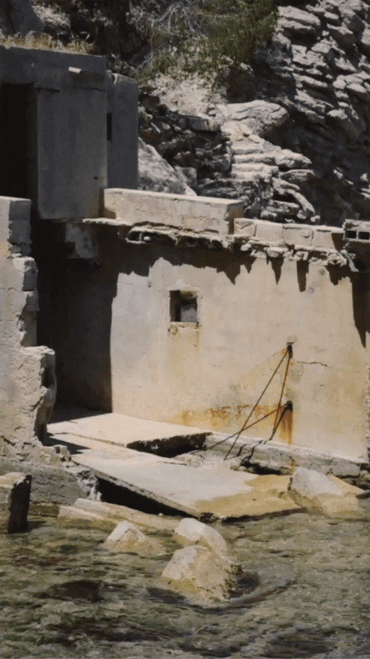 Old concrete structure built into a rocky environment with water in the foreground.