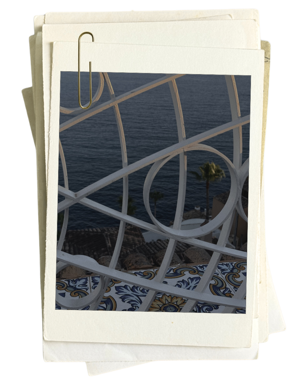 View of the ocean framed by a white decorative balcony railing, with two tall palm trees and buildings below.
