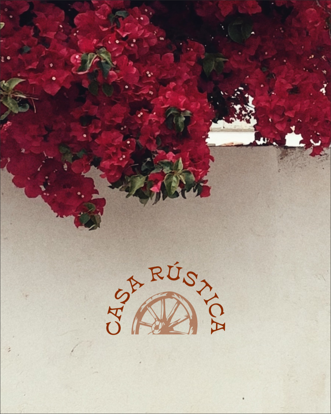 Red bougainvillea flowers hanging above a wall with a logo reading 'Casa Rústica' and an illustration of a wagon wheel.