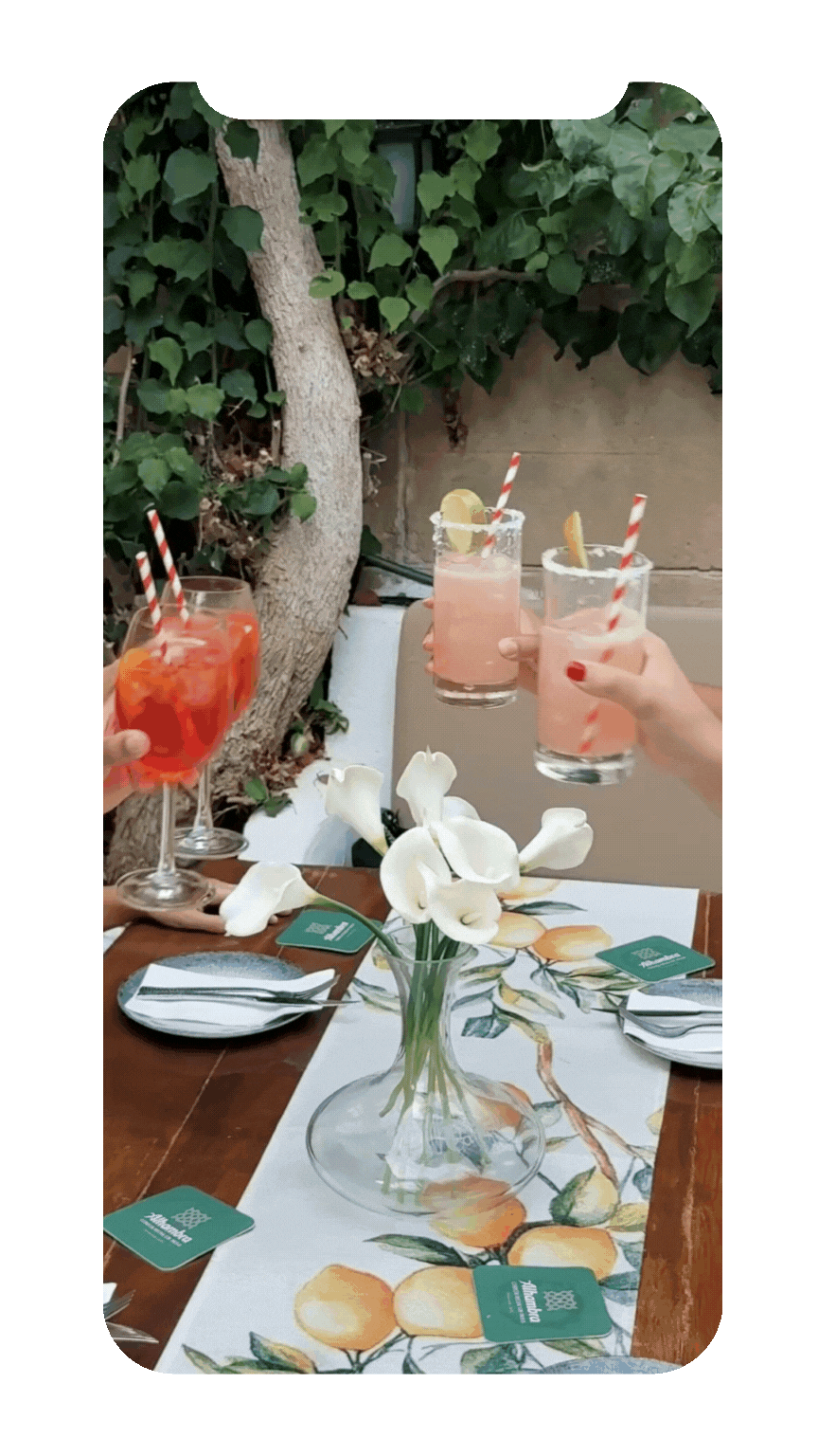 People holding pink cocktails with lemon slices and striped straws at a table with white flowers and lemon-themed table runner.