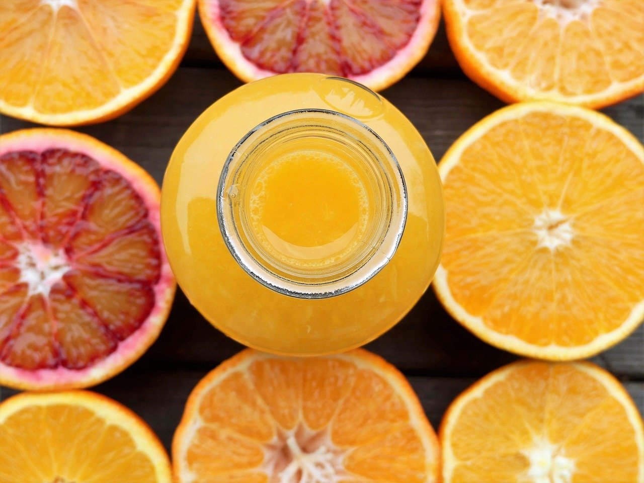 Photograph of different types of oranges cut open with a glass of fresh squeezed orange juice in the centre.
