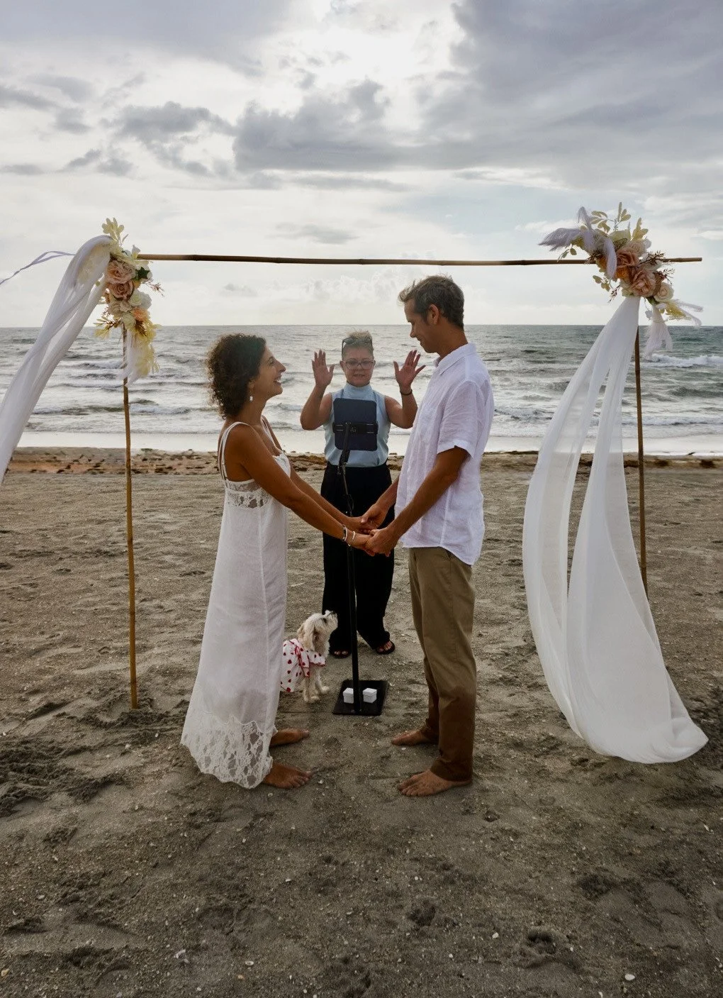 A beach wedding ceremony beneath a fabric-draped arch in Palm Beach.