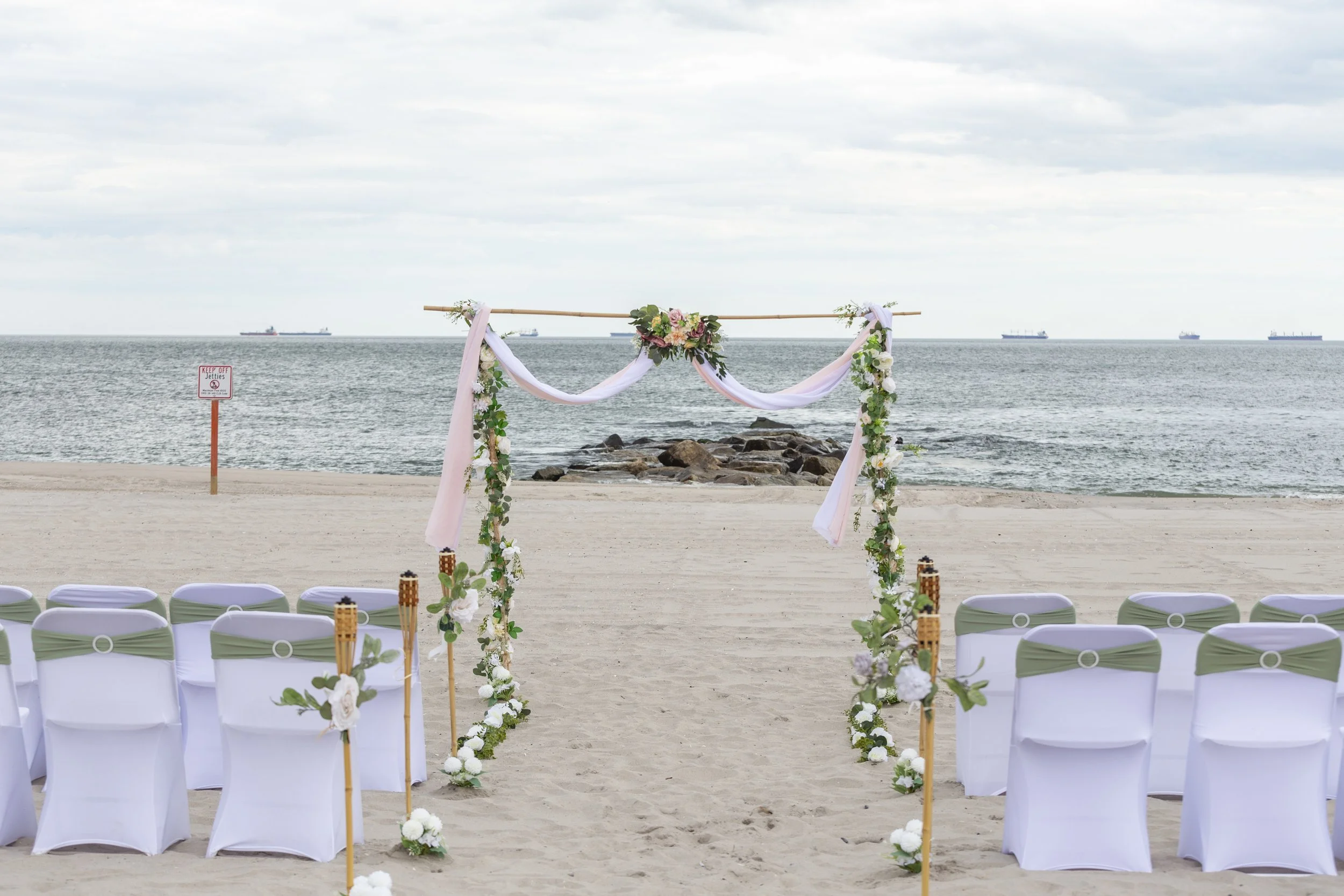 Beach wedding setup with chairs, floral arch, and ocean view