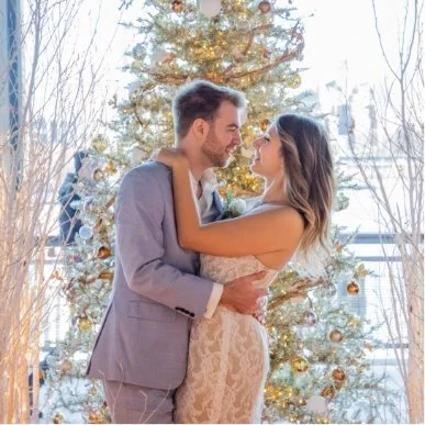 A couple embracing in front of a decorated Christmas tree with ornaments.