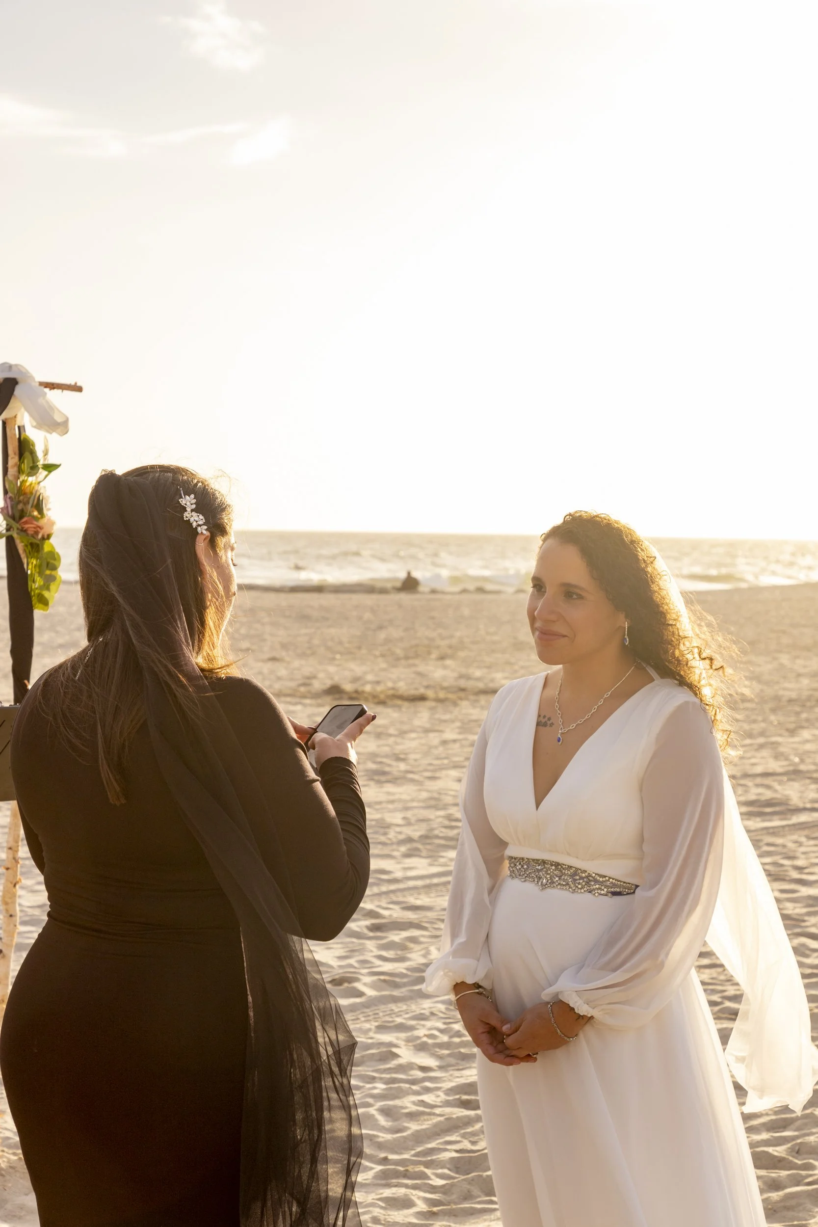 A couple facing one another during a beach wedding ceremony in warm sunset light.