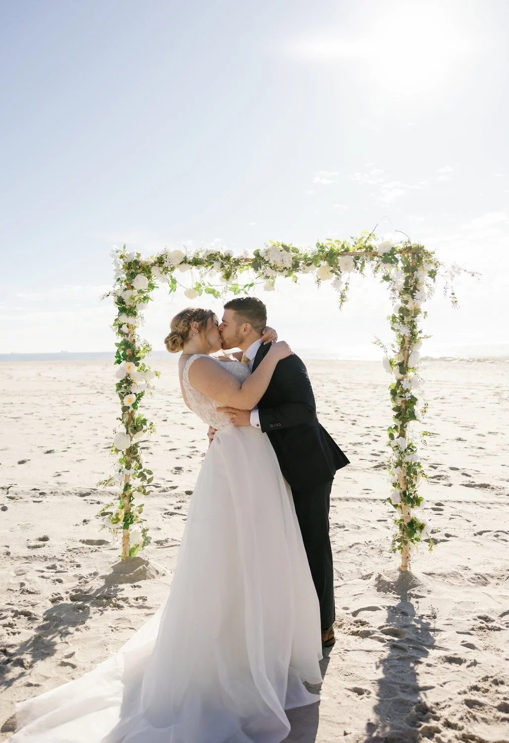 A vibrant Long Beach elopement with a happy couple kissing under wedding arch on the sand.