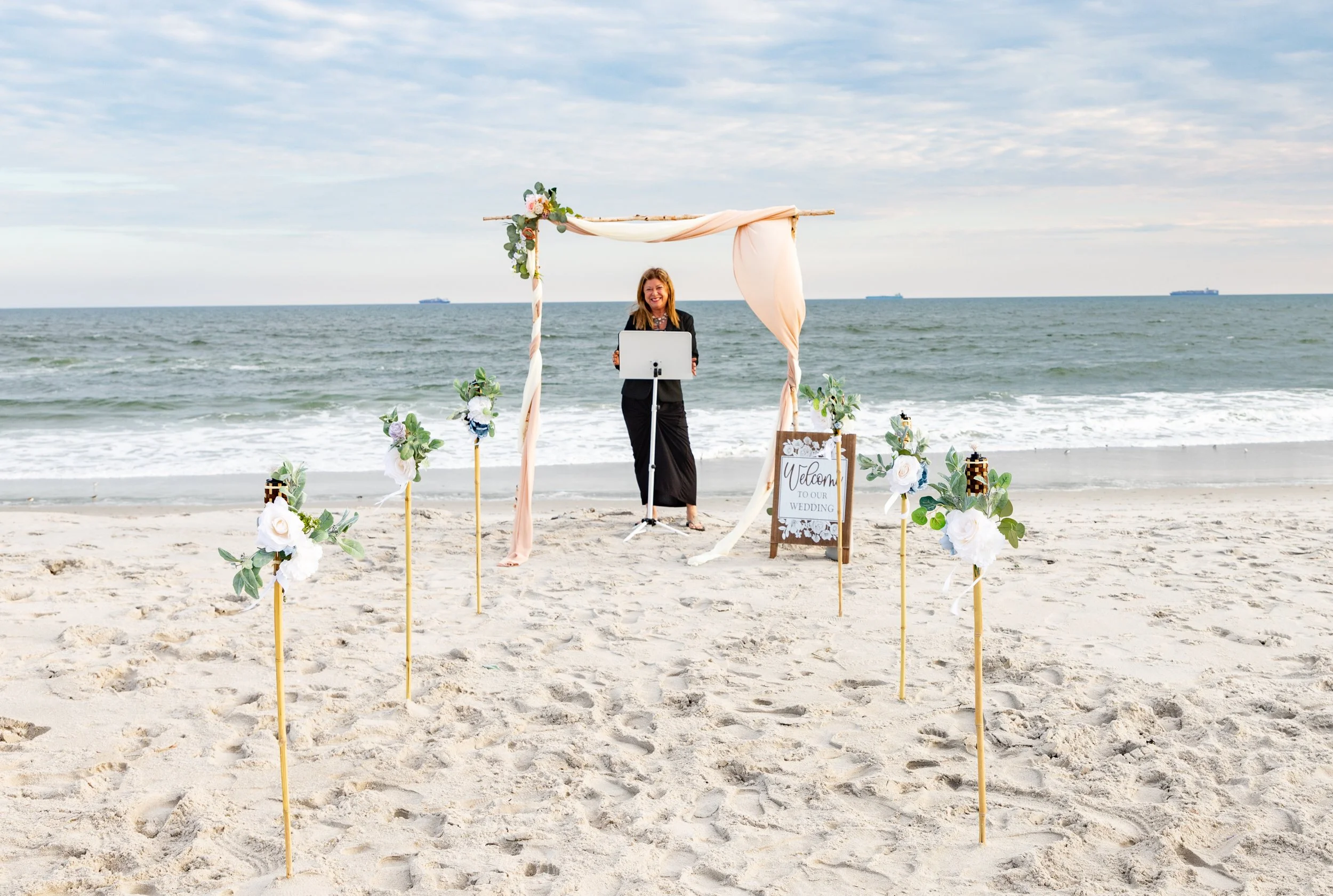 Woman standing behind a music stand on a decorated wedding arch on a beach.