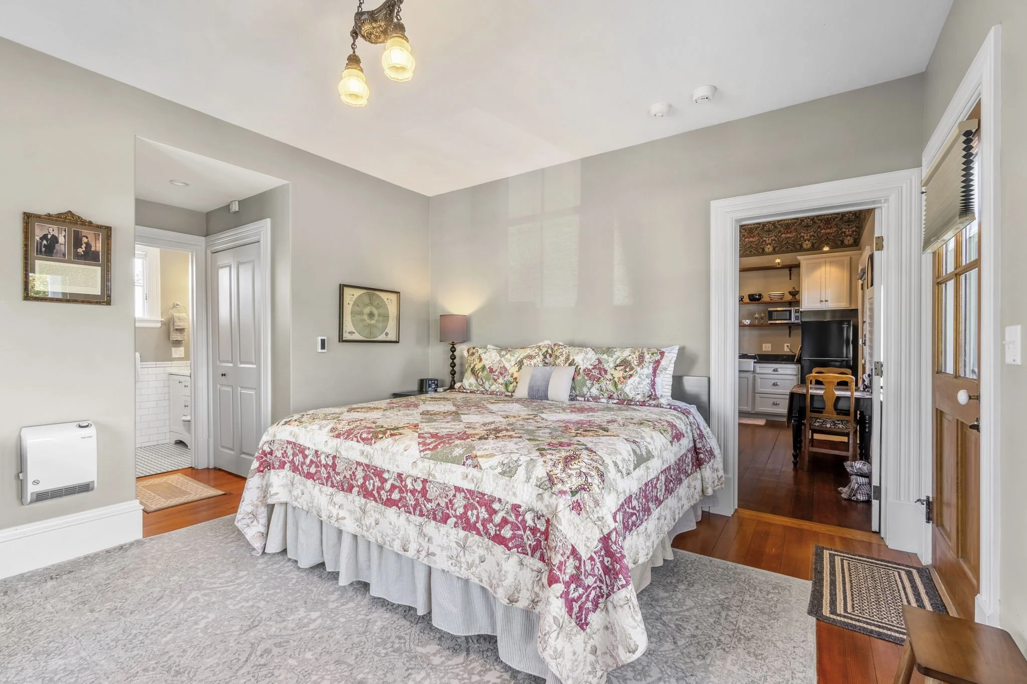 A bedroom with a large bed, pink lamps, a wooden nightstand, a desk by the window, green walls, and hardwood floors.