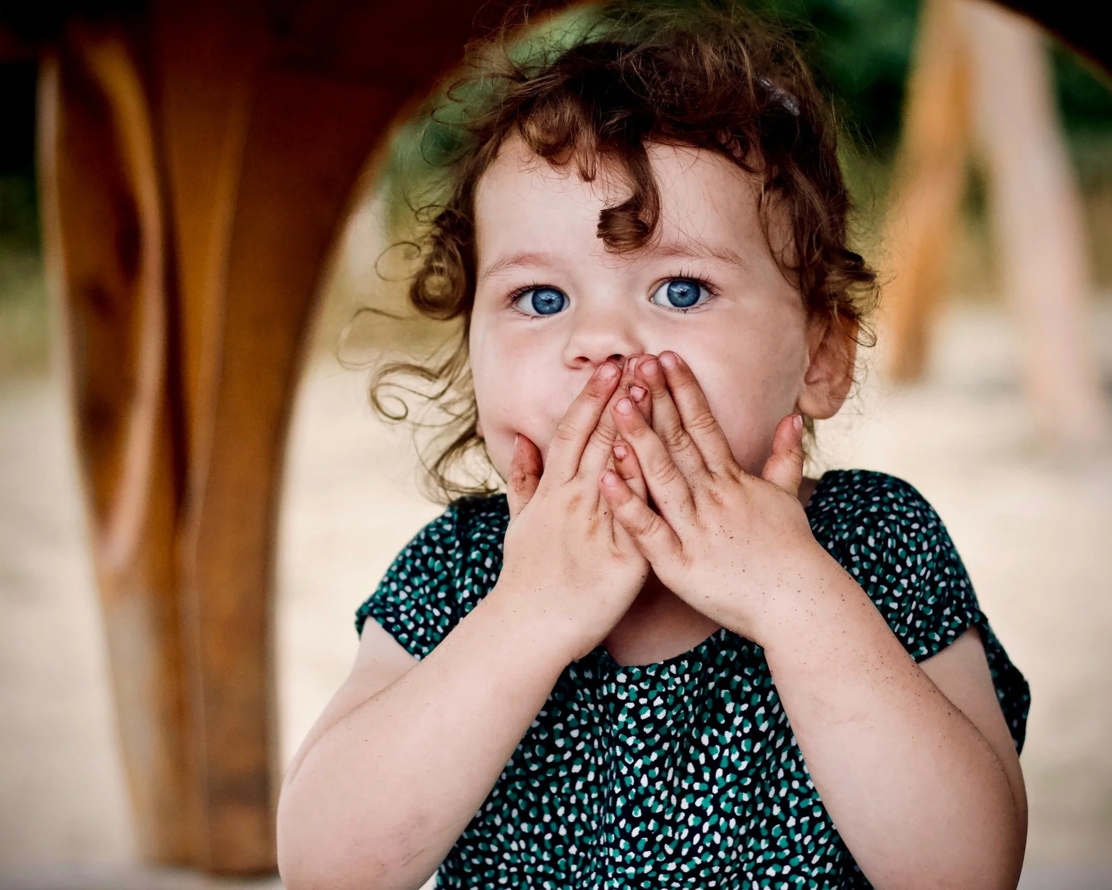 a girl with a green shirt and curly hair covering her mouth with her hands