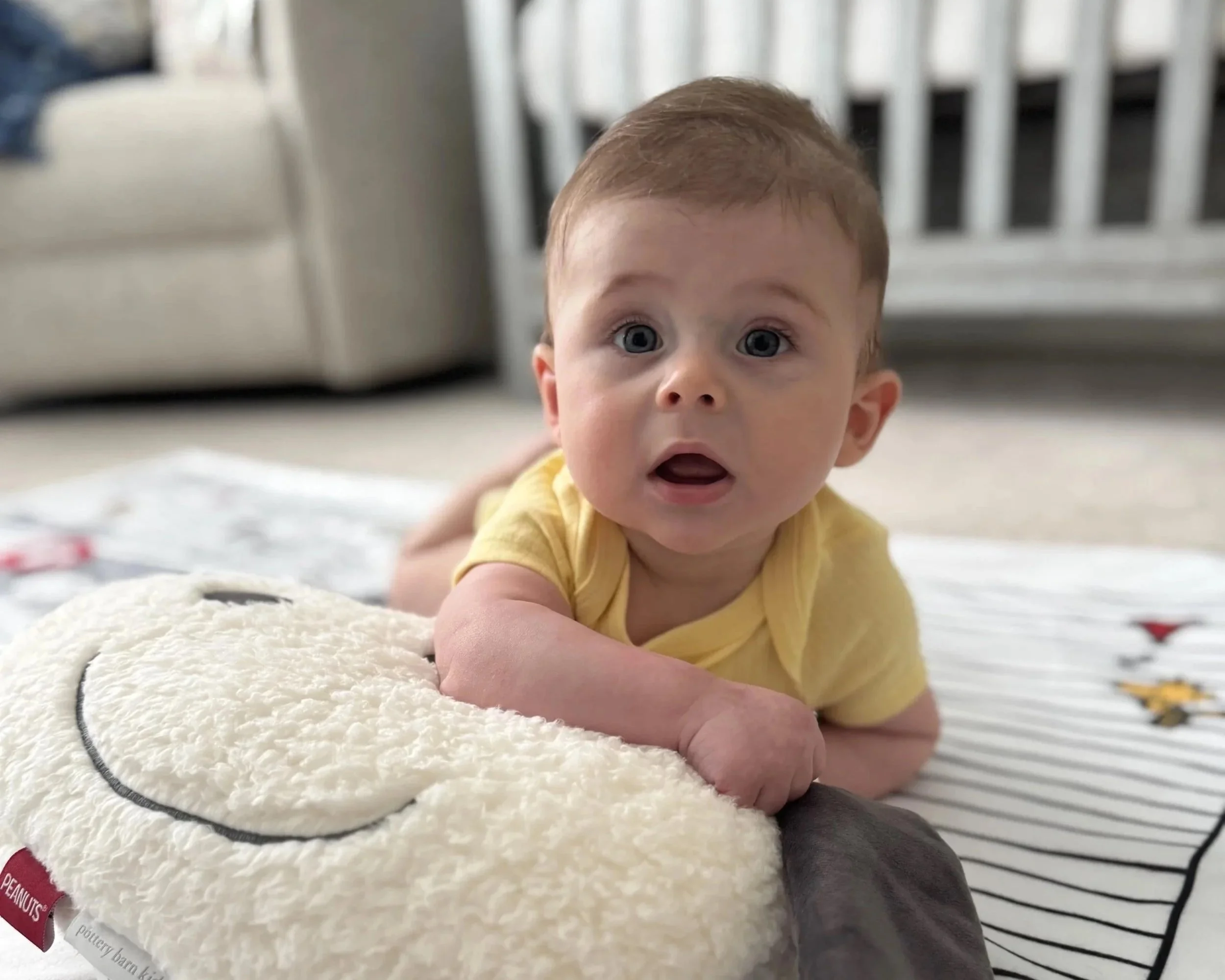 a baby boy in a yellow shirt laying on his belly and looking up
