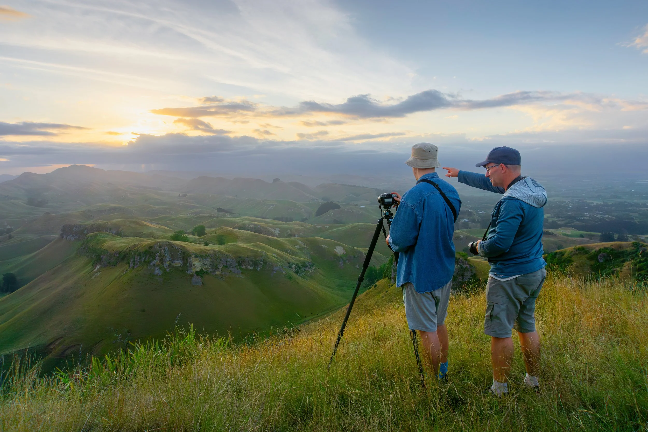 Jos Buurmans guiding a Camera Foundations participant on a tripod-mounted shot over Hawke's Bay's rolling hill country, early morning light from Te Mata Peak.