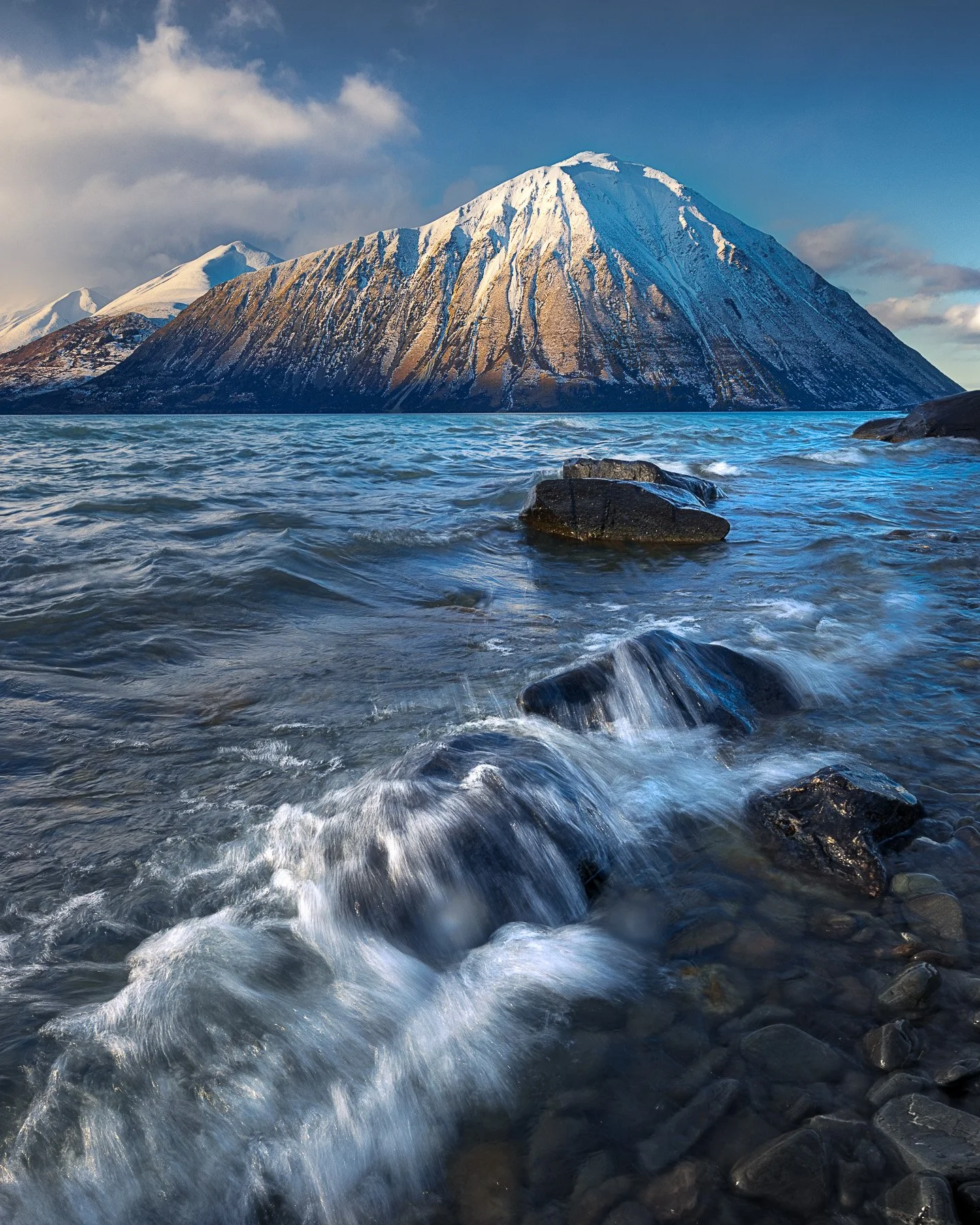 Wave breaking over shoreline rocks beneath the triangular Ben Ohau Range at Lake Ōhau, New Zealand