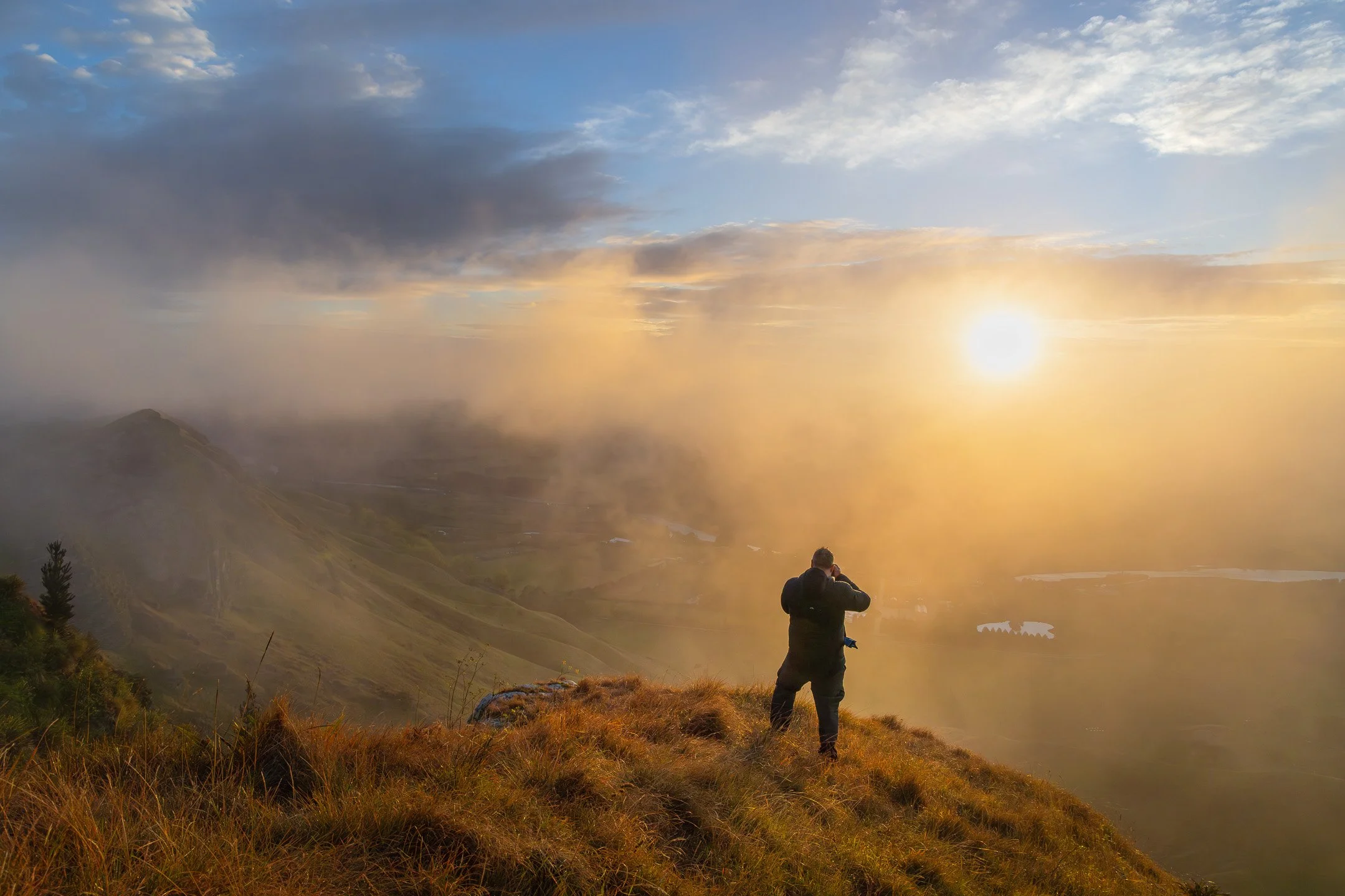 A photographer working backlit fog and low sun on a Hawke's Bay ridgeline — the kind of shifting, unpredictable conditions a Seeing the Landscape session is built around.