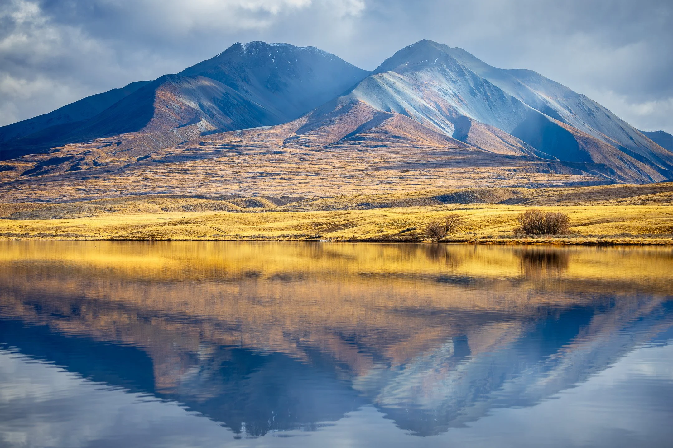 The twin mountain peaks of Mount Potts in the Potts Range perfectly reflected in the calm, mirrored water of Lake Clearwater in Canterbury, New Zealand