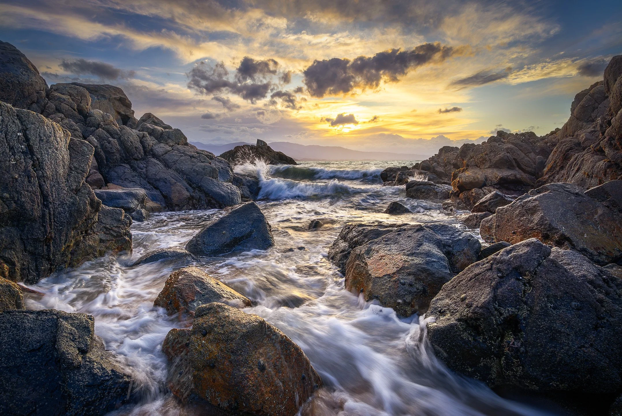Low angled golden hour light warms the rocks and incoming tide at Tata Beach, waves folding around the shoreline in rhythmic motion, Tasman Region, New Zealand.