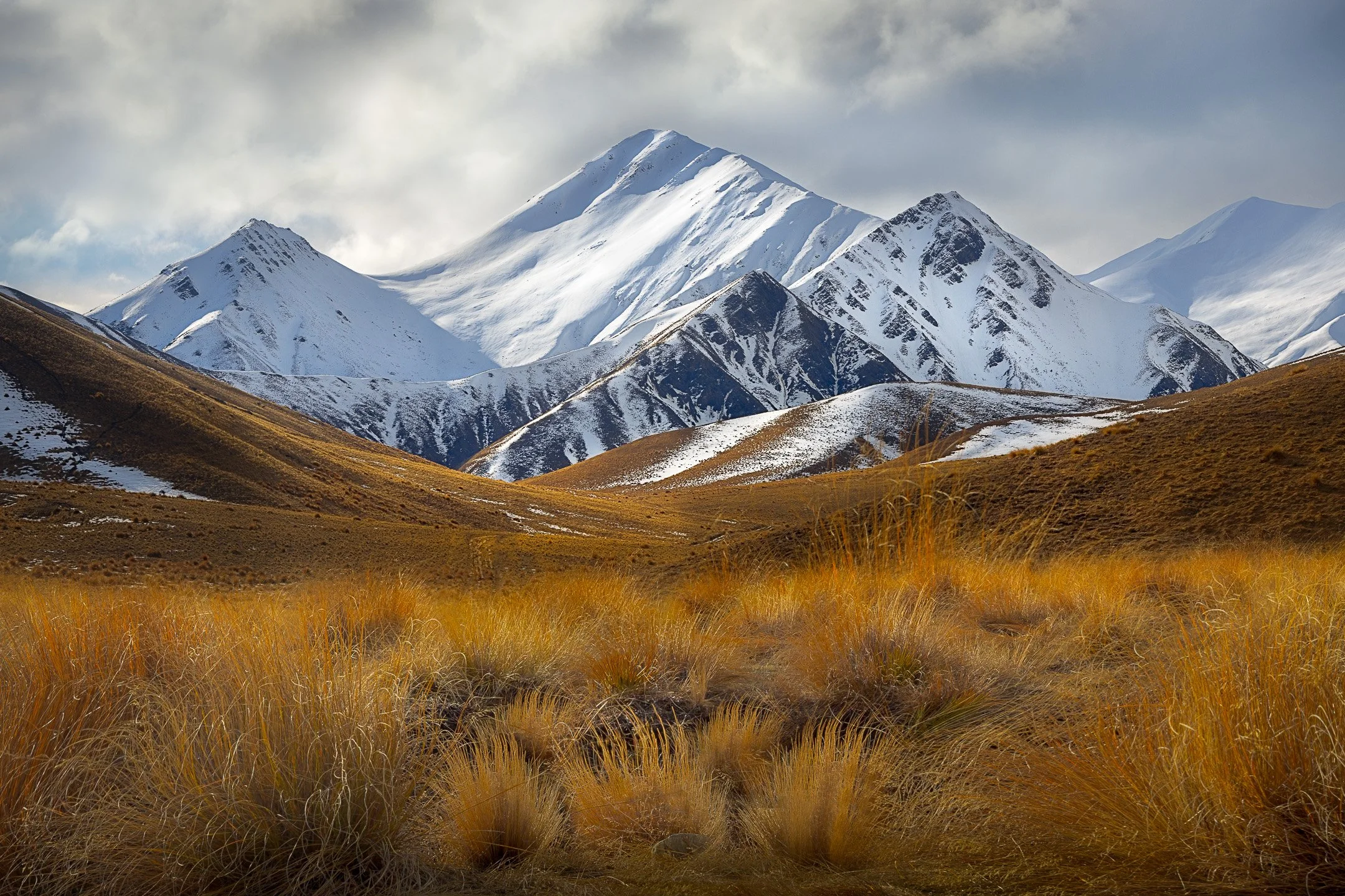 Snow-dusted triangular peaks above glowing tussock grass at Lindis Pass, New Zealand