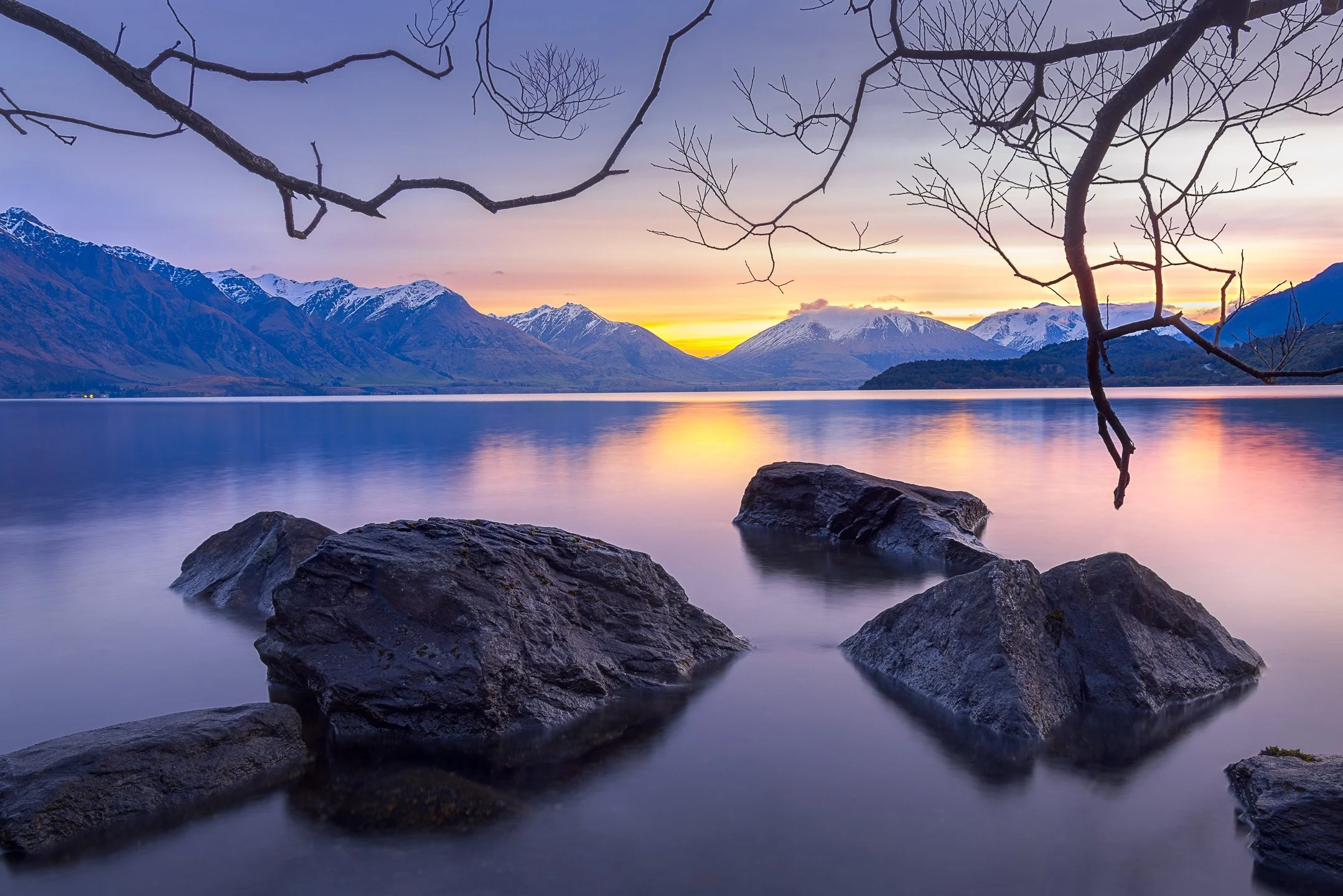 A calm Wilson Bay at Lake Wakatipu holds the last warm colours of a tranquil sunset, the still water reflecting the fading light and distant ranges, Otago, New Zealand.